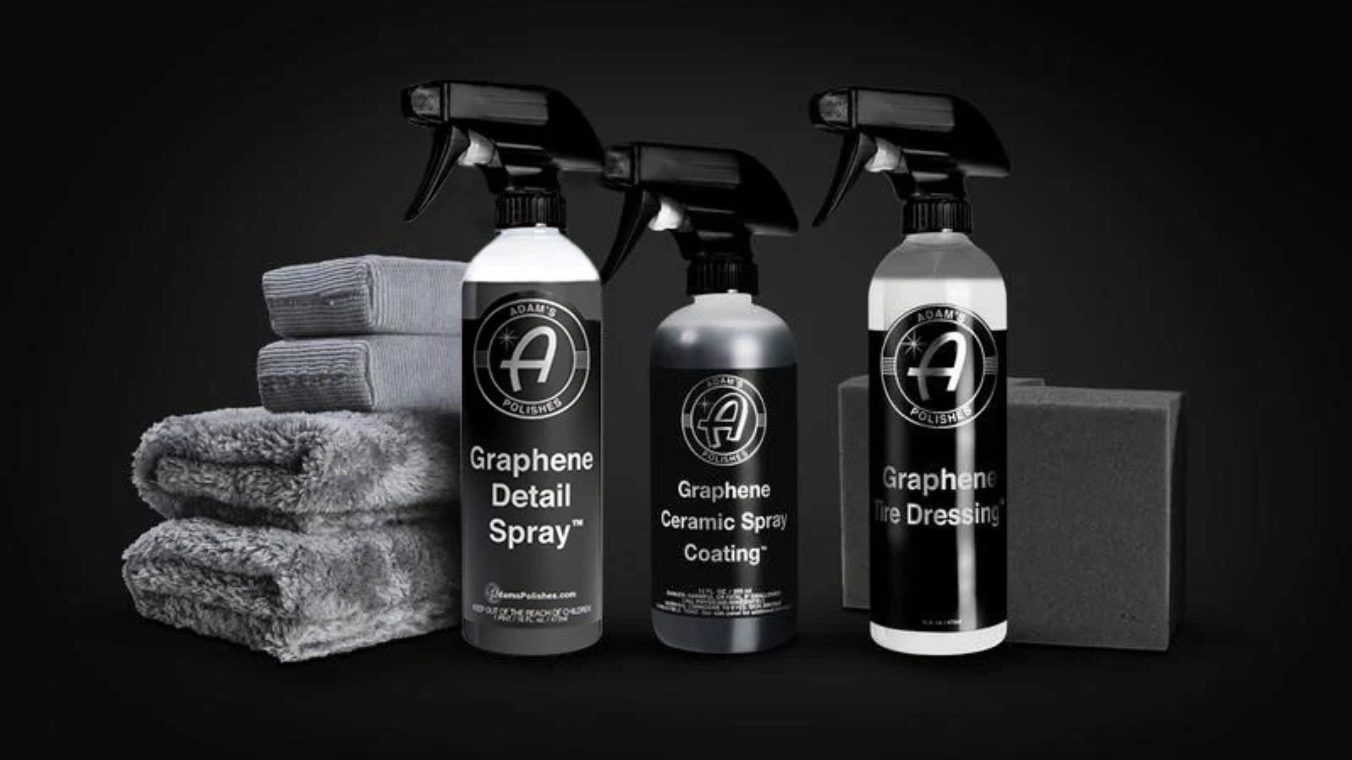 Three bottles of Adam's Polishes graphene car care products with gray microfiber towels and a sponge on a dark background.