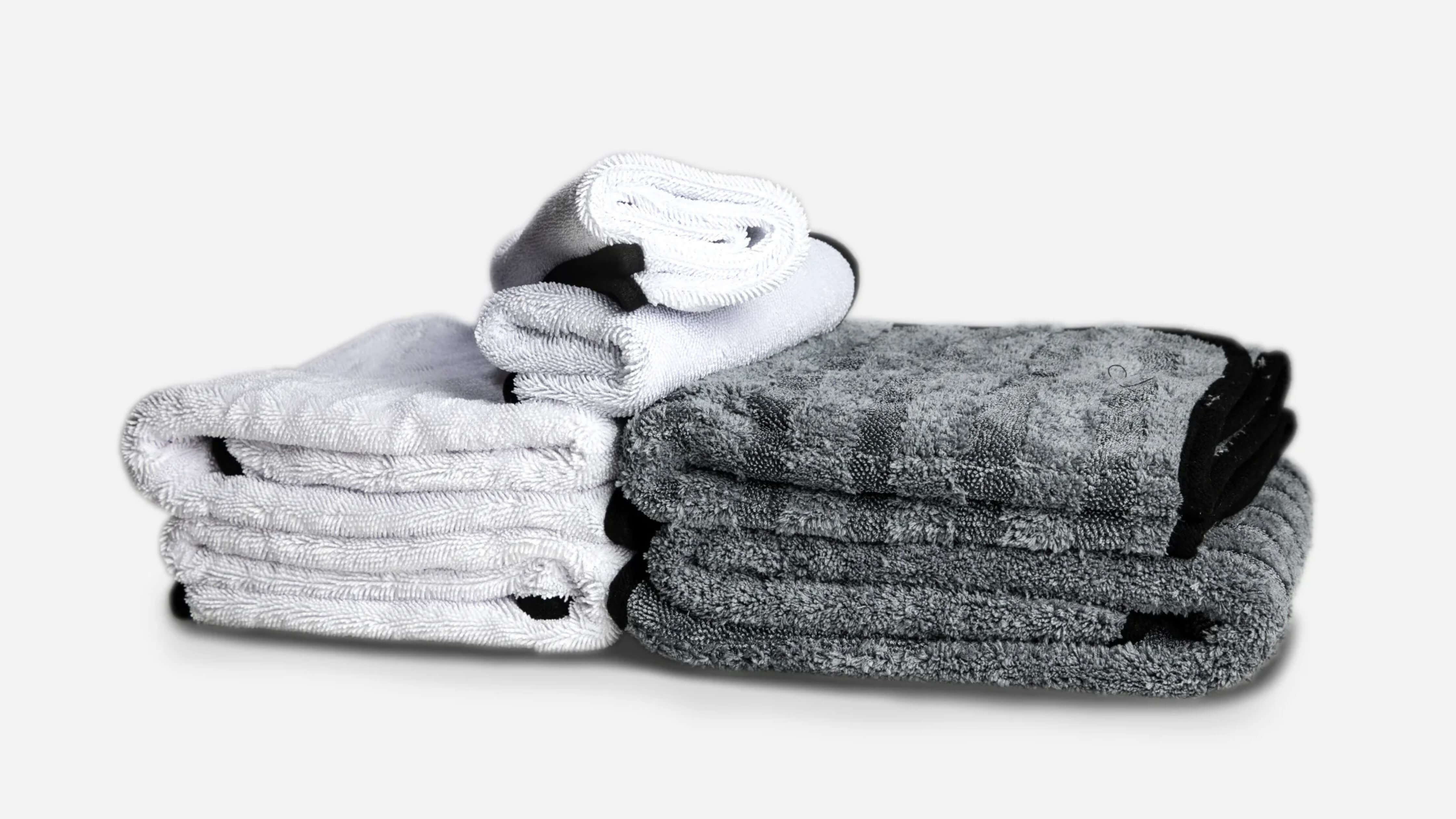 Two stacks of folded microfiber towels, one white and one gray, with a smaller rolled towel on top, ideal for car detailing.