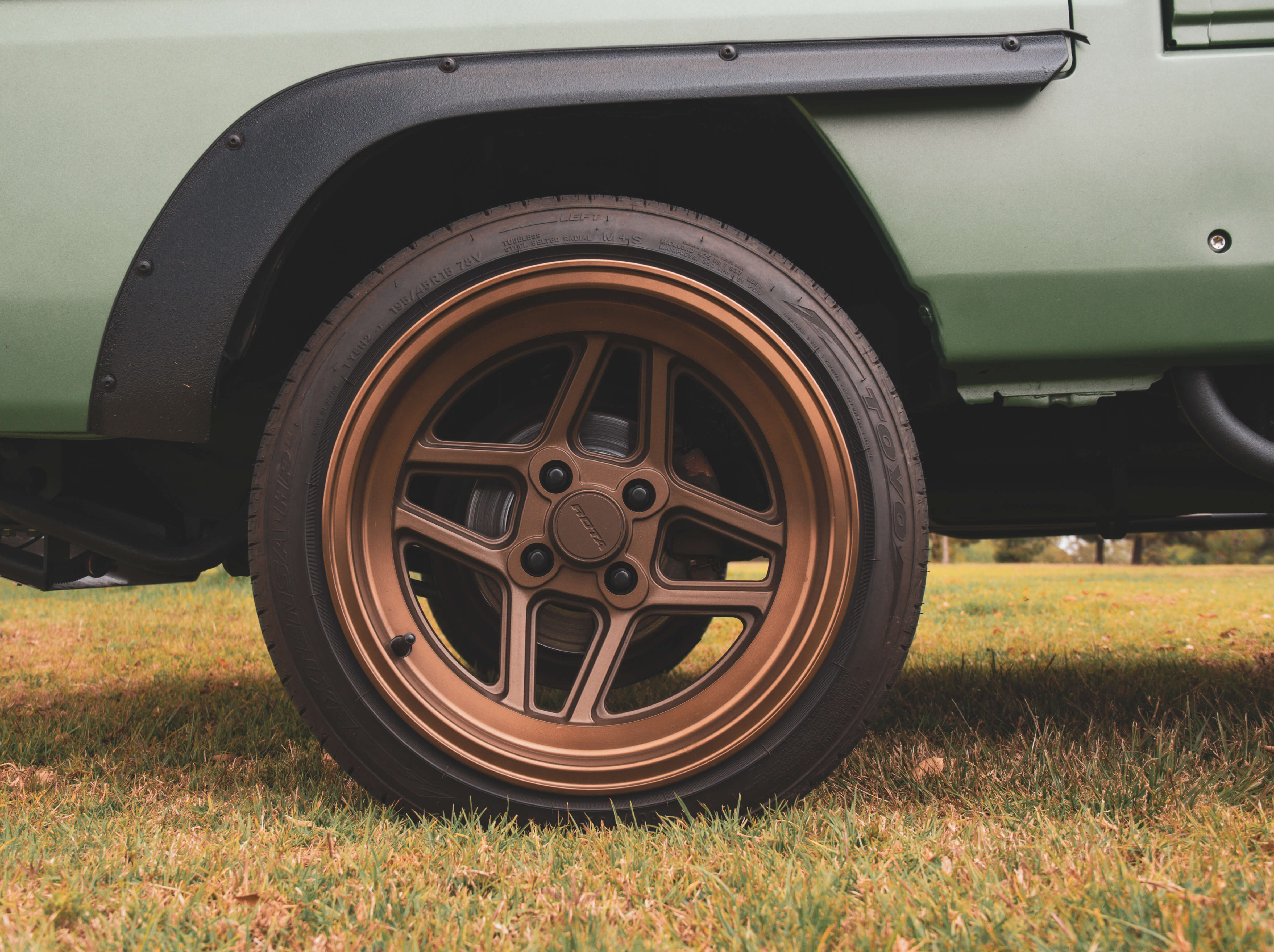 Close-up side view of a bronze aftermarket wheel with 4x100 lug pattern mounted on a customized Honda Acty truck, showcasing ideal fitment and tire clearance.