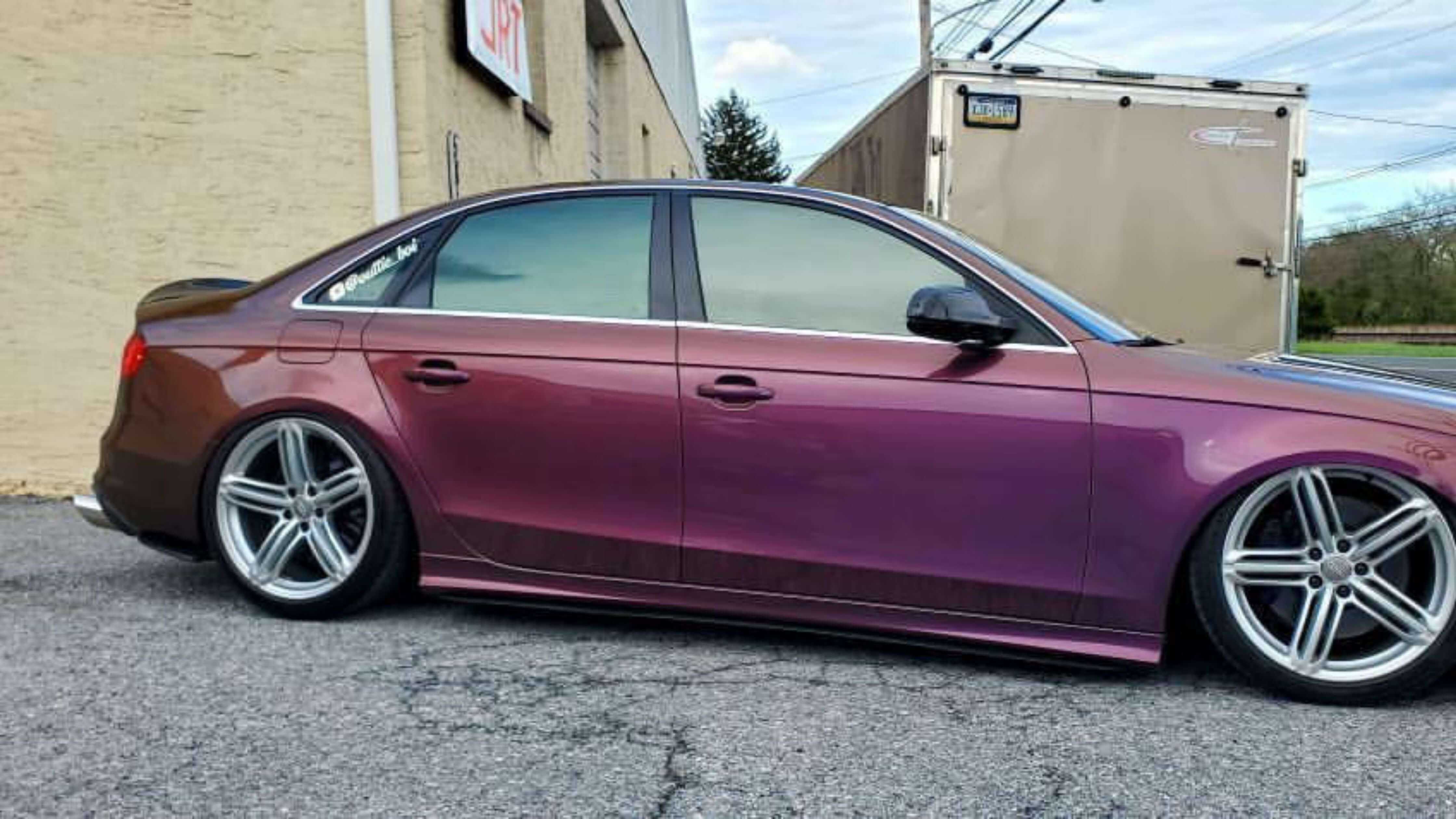 A purple car with a low stance and large silver wheels parked on a street next to a beige building, illustrating leased car tinting options.