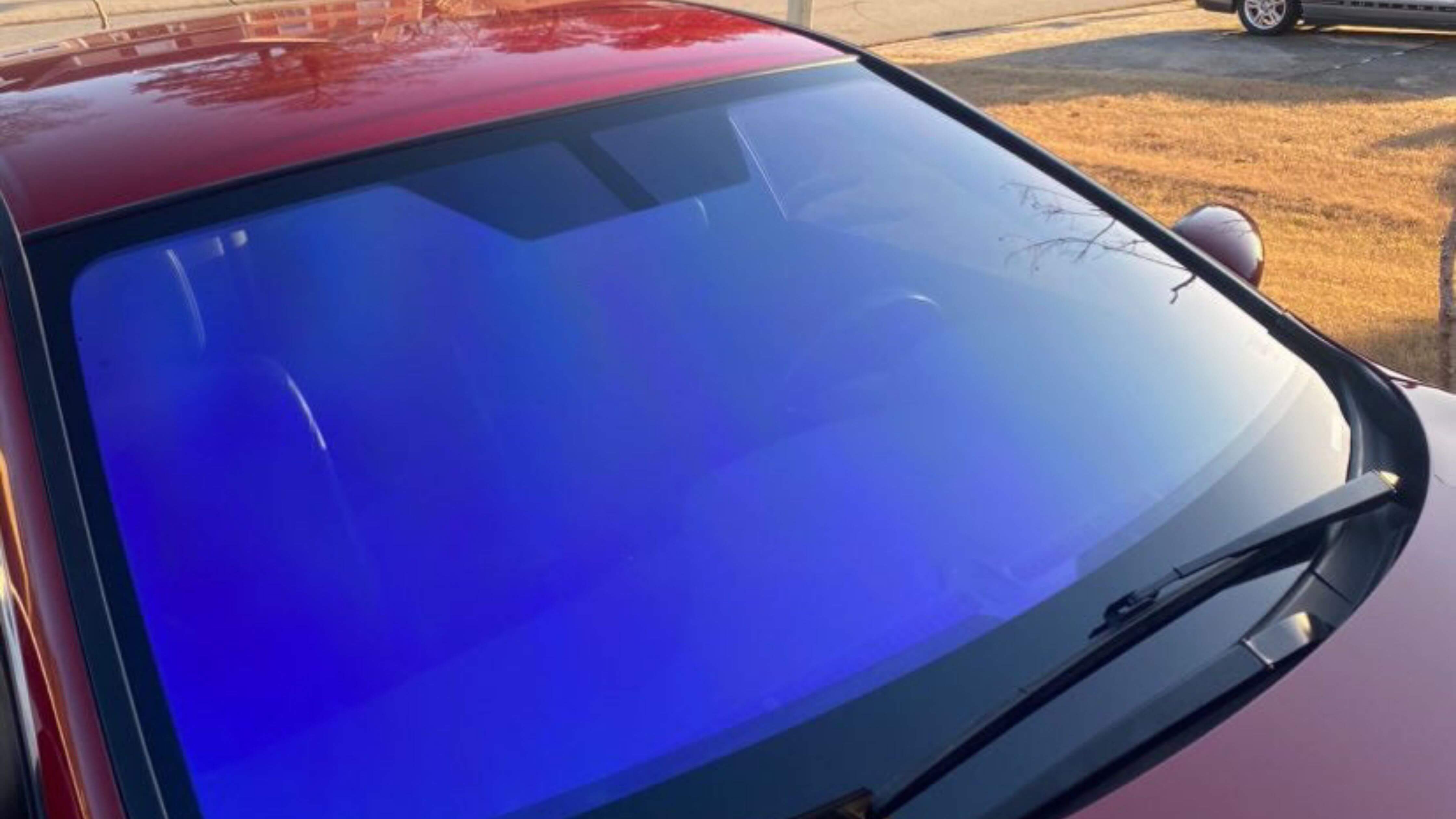 A red car with blue tint effect on windshield parked in sunlight.