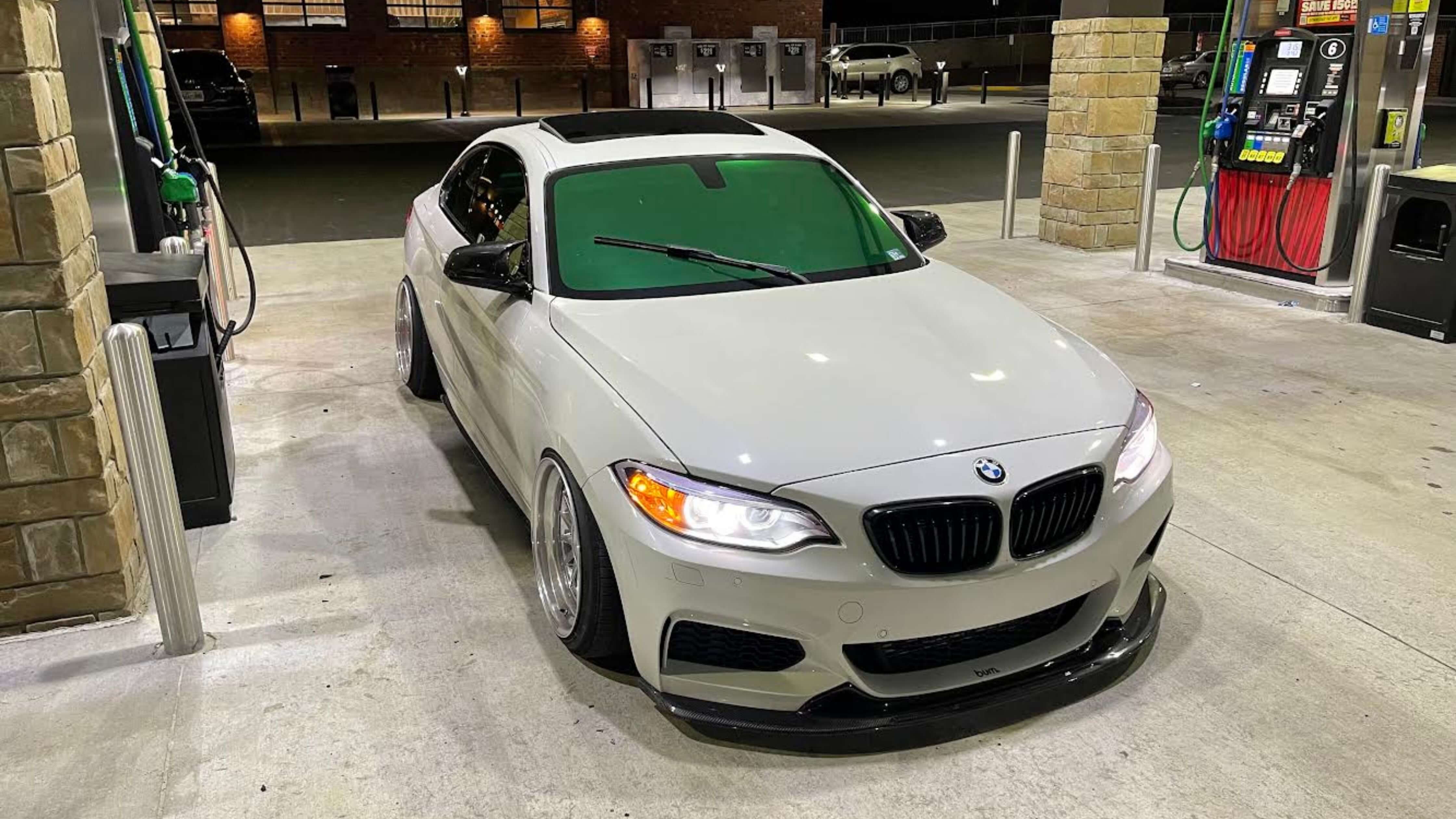A white BMW with tinted windows parked at a gas station, showcasing legal tinting options for leased cars.