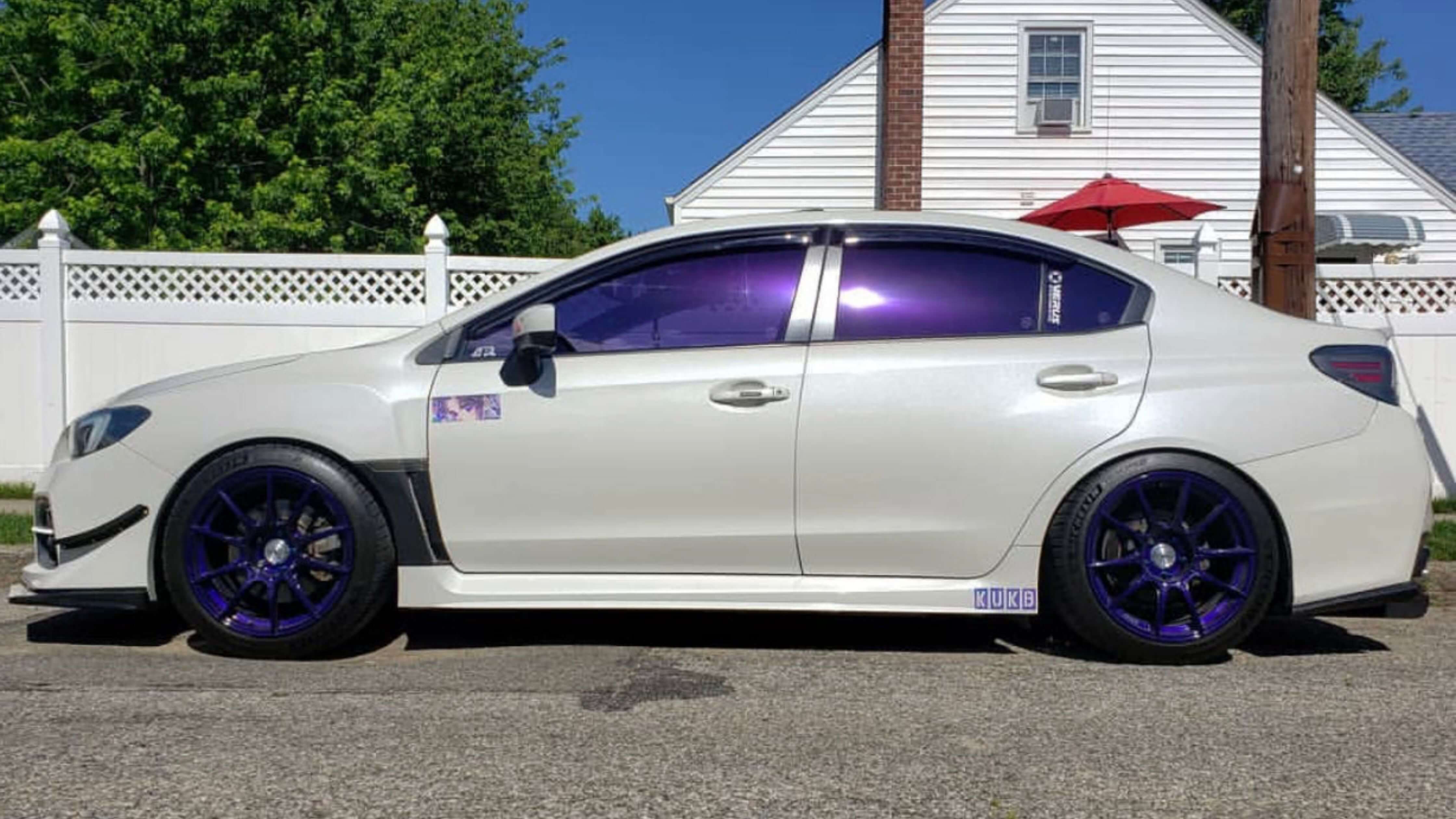 A white sedan with purple-tinted windows parked on a street, showcasing stylish car tint options.