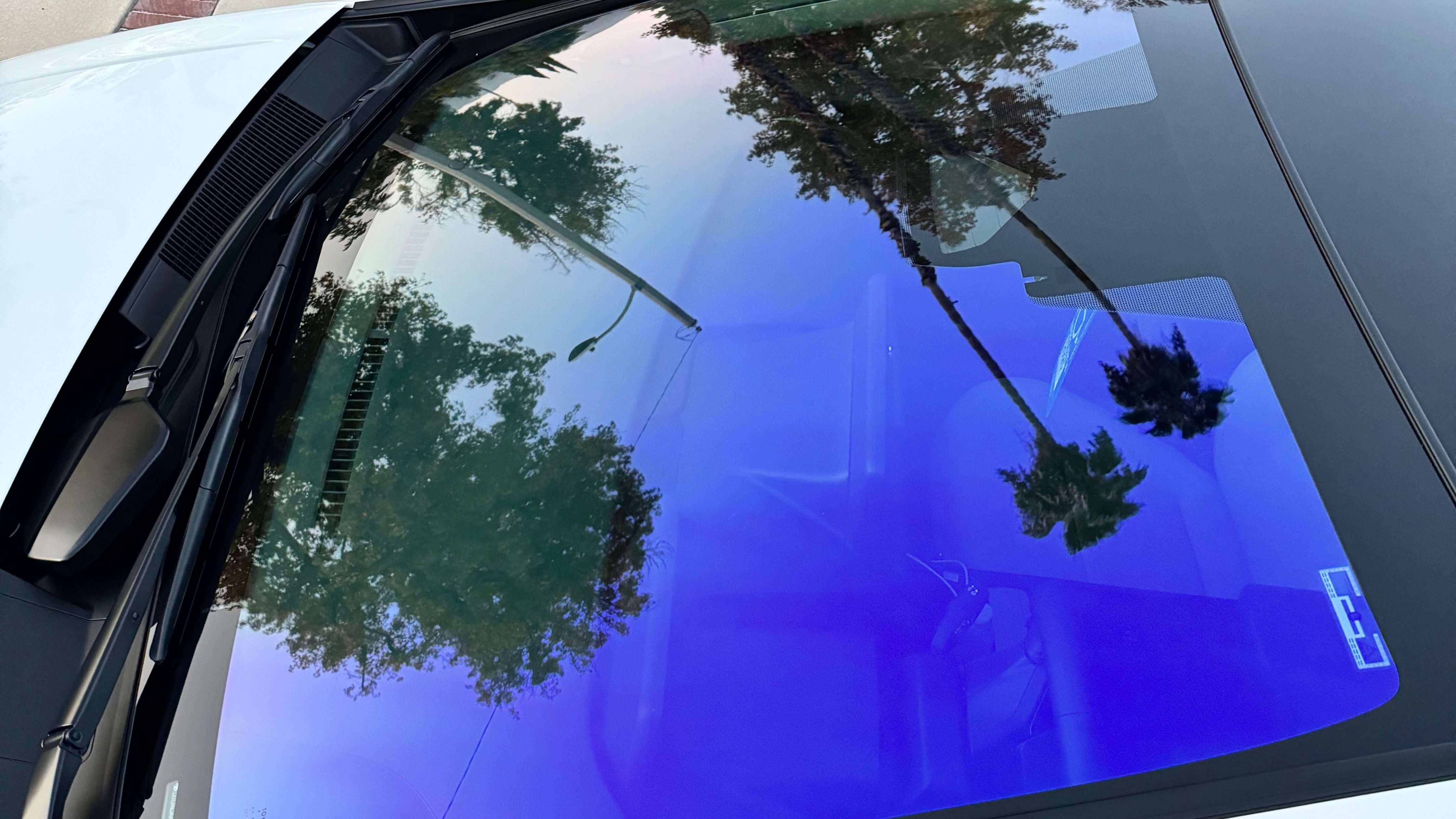 Car with mirror window tint reflecting trees and streetlamp, showcasing stylish privacy.