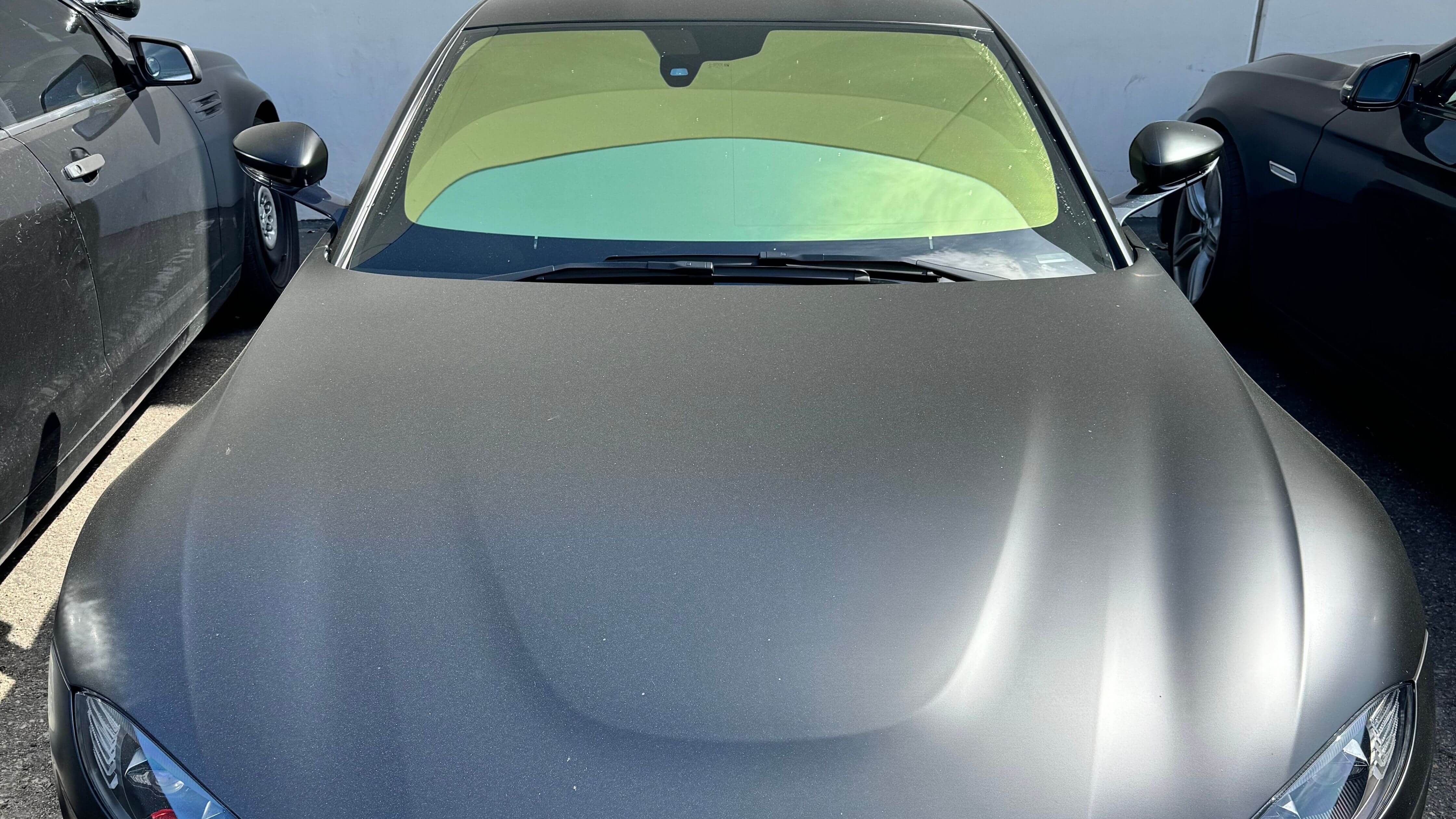 Matte black car with green sunshade on windshield showcasing window tint benefits.