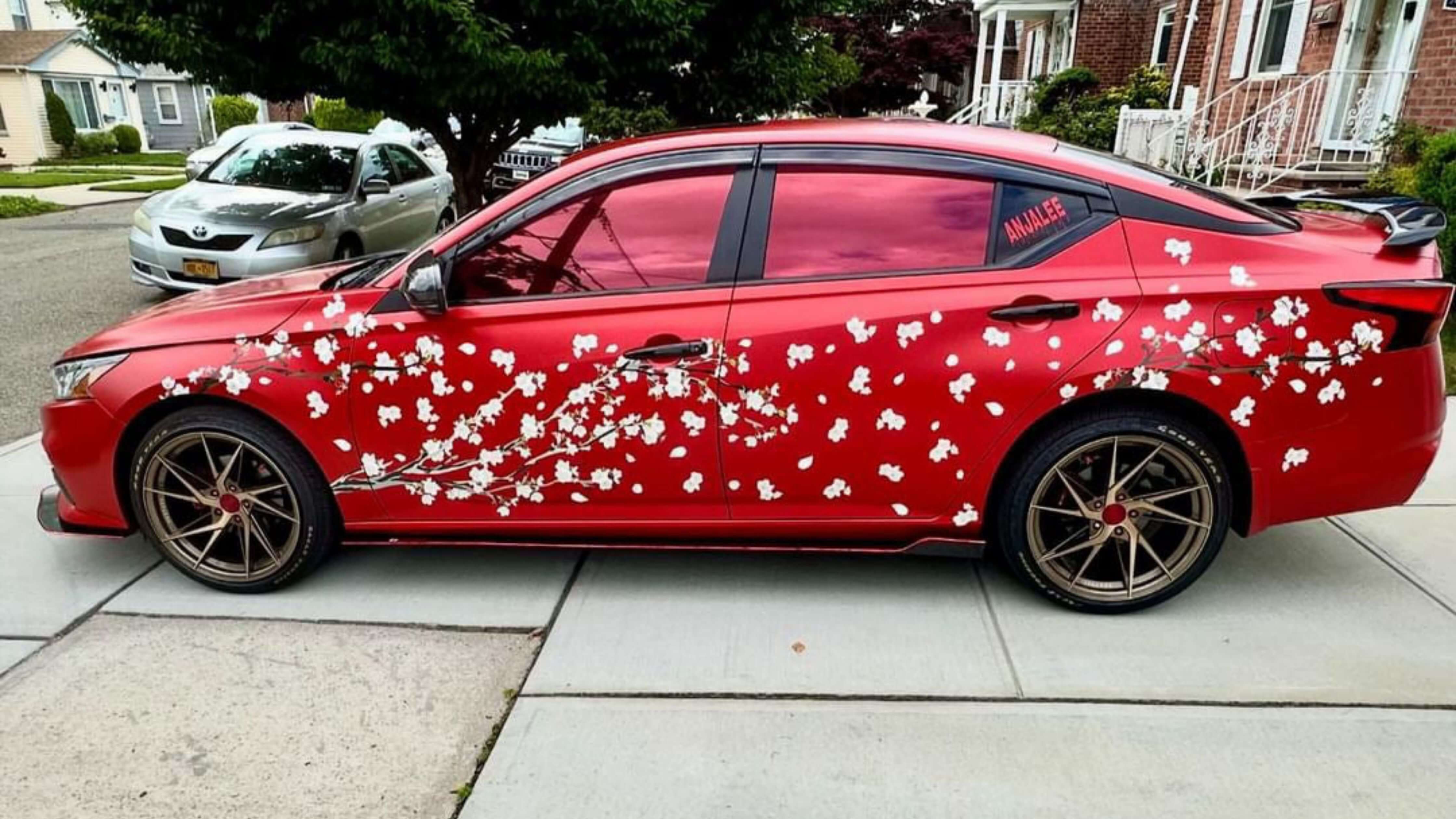 A red car with a cherry blossom design on its side is parked on a residential street, showcasing freshly tinted windows.