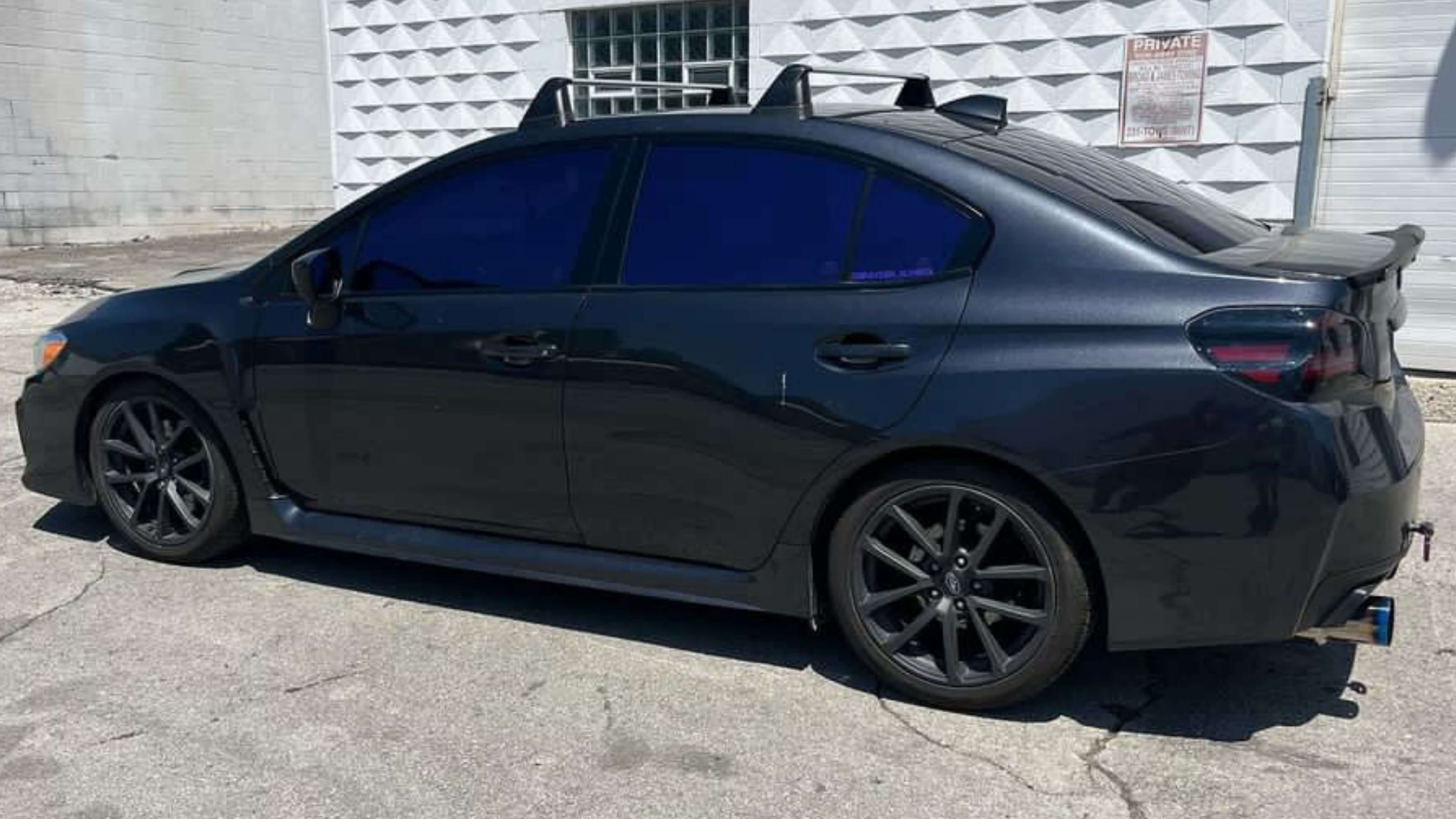 Black sedan with tinted windows parked on concrete near a textured wall.