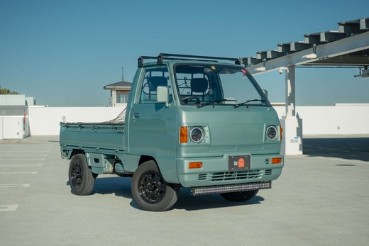 Green Kei Truck Parked in a Sunlit Lot with a Clear Blue Sky Background