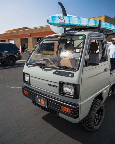 Lifted Kei Truck with Surfboards on Roof Rack, Parked Outdoors on a Sunny Day