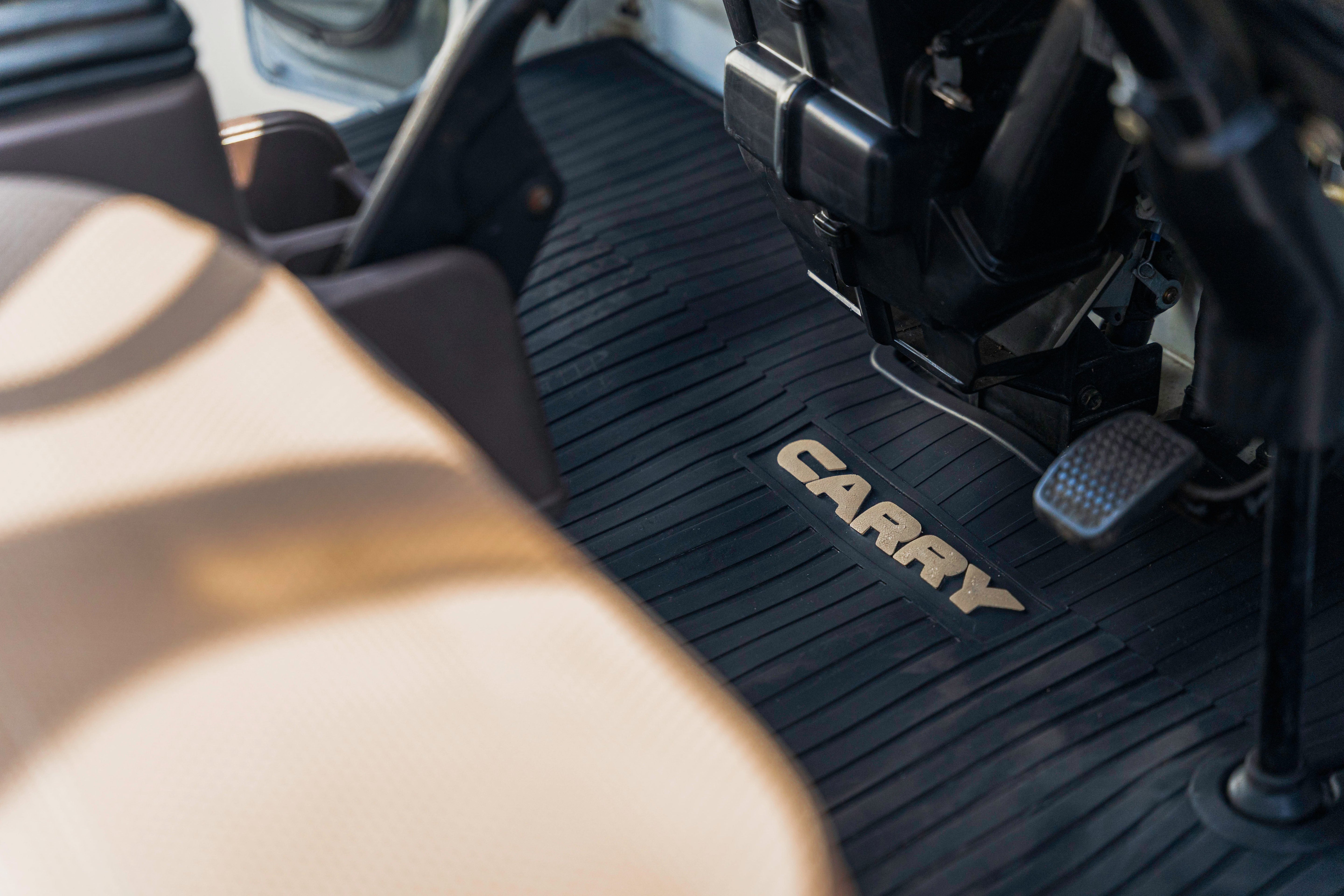 Close-up of a vehicle's interior showing a black floor mat with the word "CARRY" and a pedal.