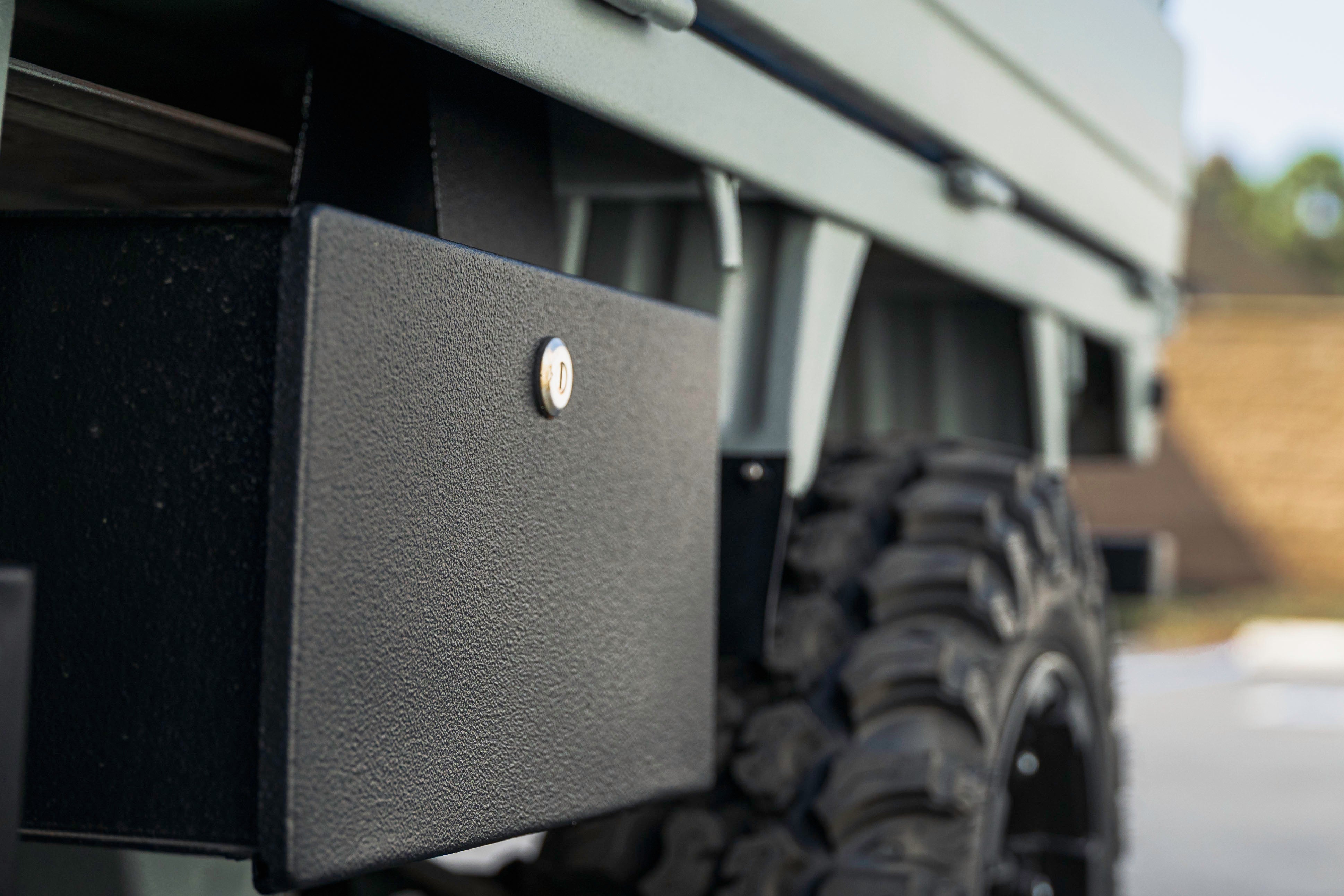 Close-up of a rugged vehicle's side, showing a textured black storage box and a large off-road tire.