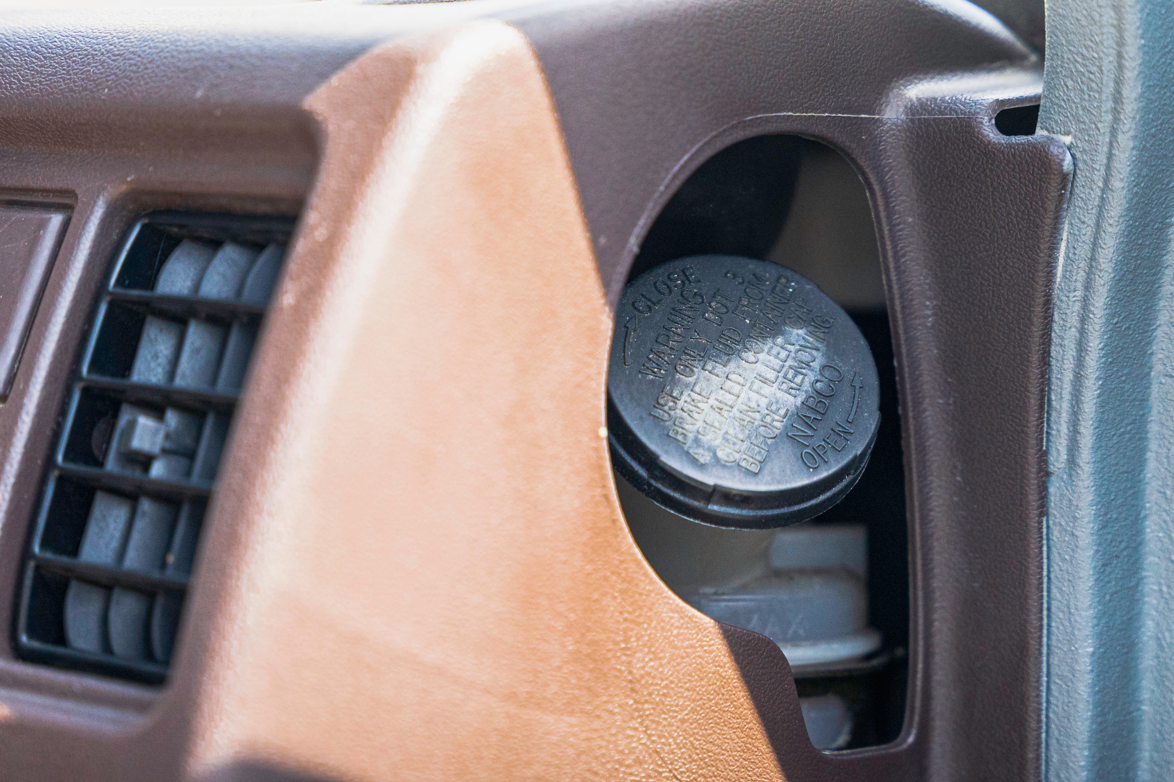 A close-up of a car's dashboard showing a brake fluid reservoir cap with warning text.