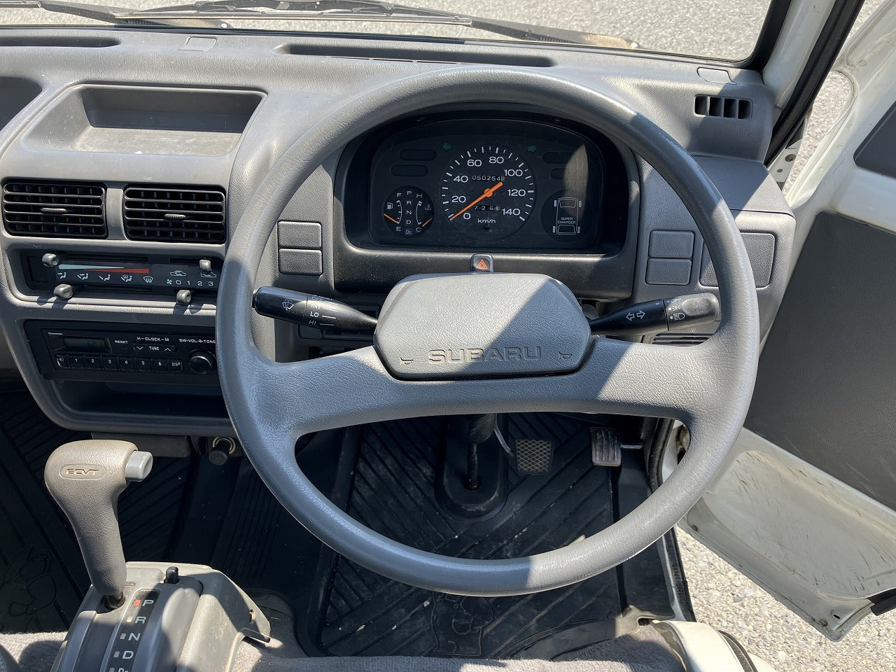 Interior view of a vehicle's dashboard featuring a Subaru steering wheel, speedometer, gear shift, and control panel.