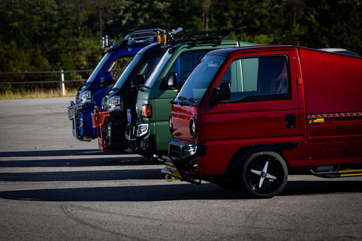 A row of lowered Honda Acty mini trucks lined up, each featuring customized suspension, aerodynamic enhancements, and distinctive styling elements that improve handling, road stance, and overall street performance.