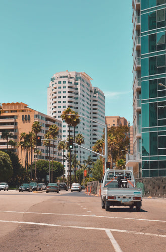 Kei Truck Driving in a City with High-Rise Buildings and Palm Trees