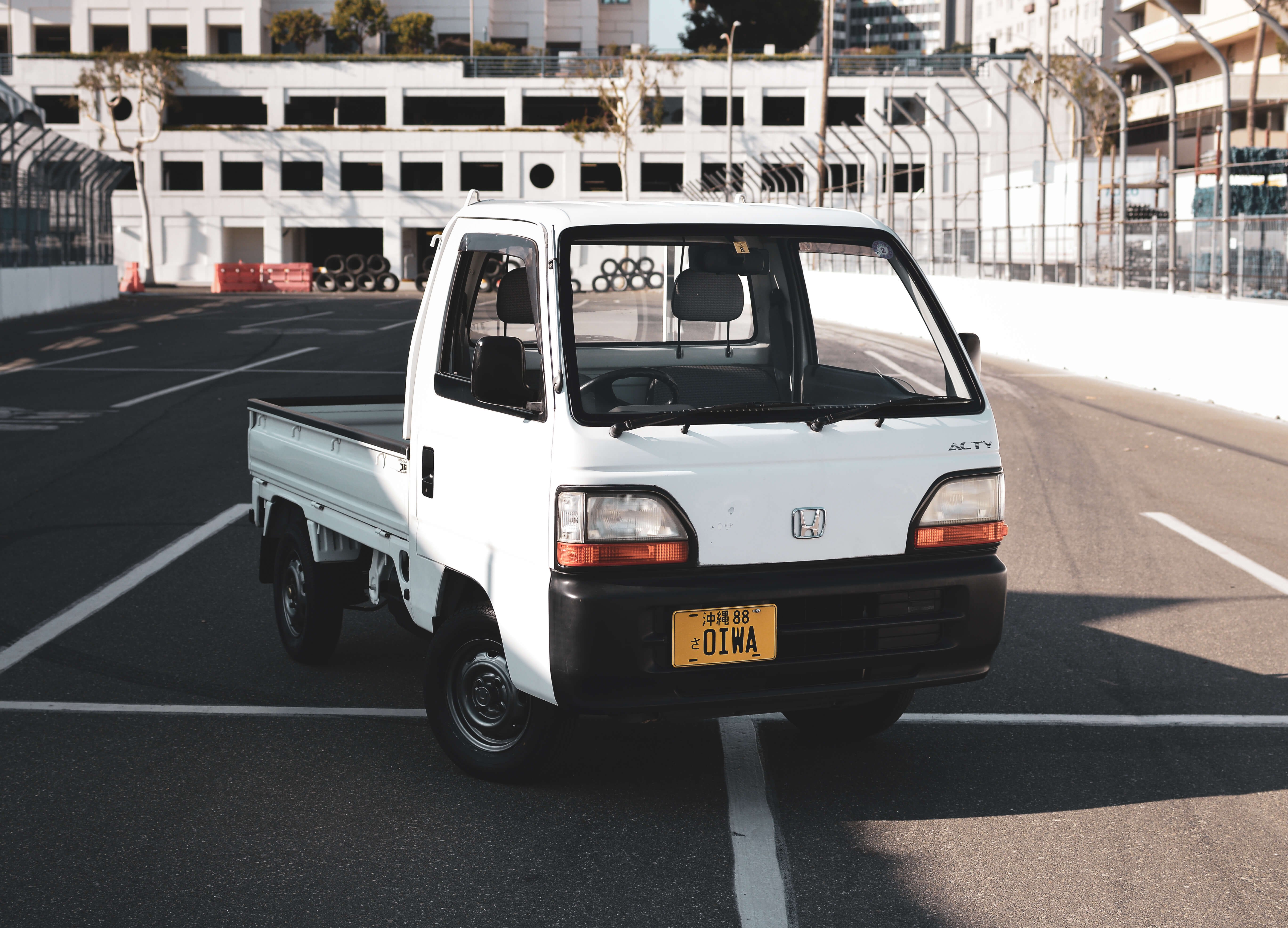 Front view of a white Honda Acty Truck parked on a racetrack, showcasing its compact design and connection to Oiwa Garage’s reliable Honda Acty Parts for maintenance and restoration.