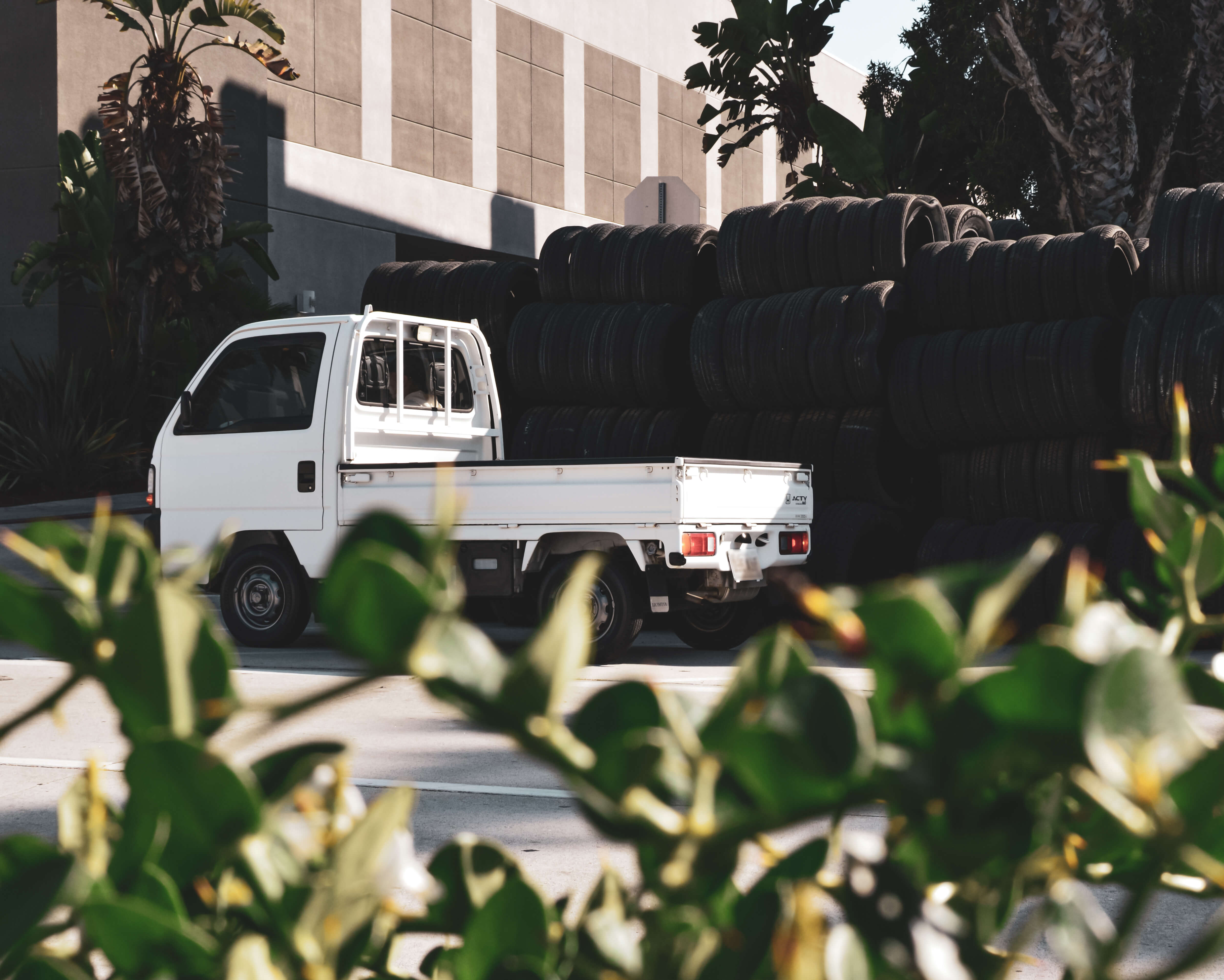 Side View of Honda Acty Kei Truck Next to Stacked Tires - Pronouncing ‘Kei Truck’ Correctly and Appreciating Its Cultural Significance.