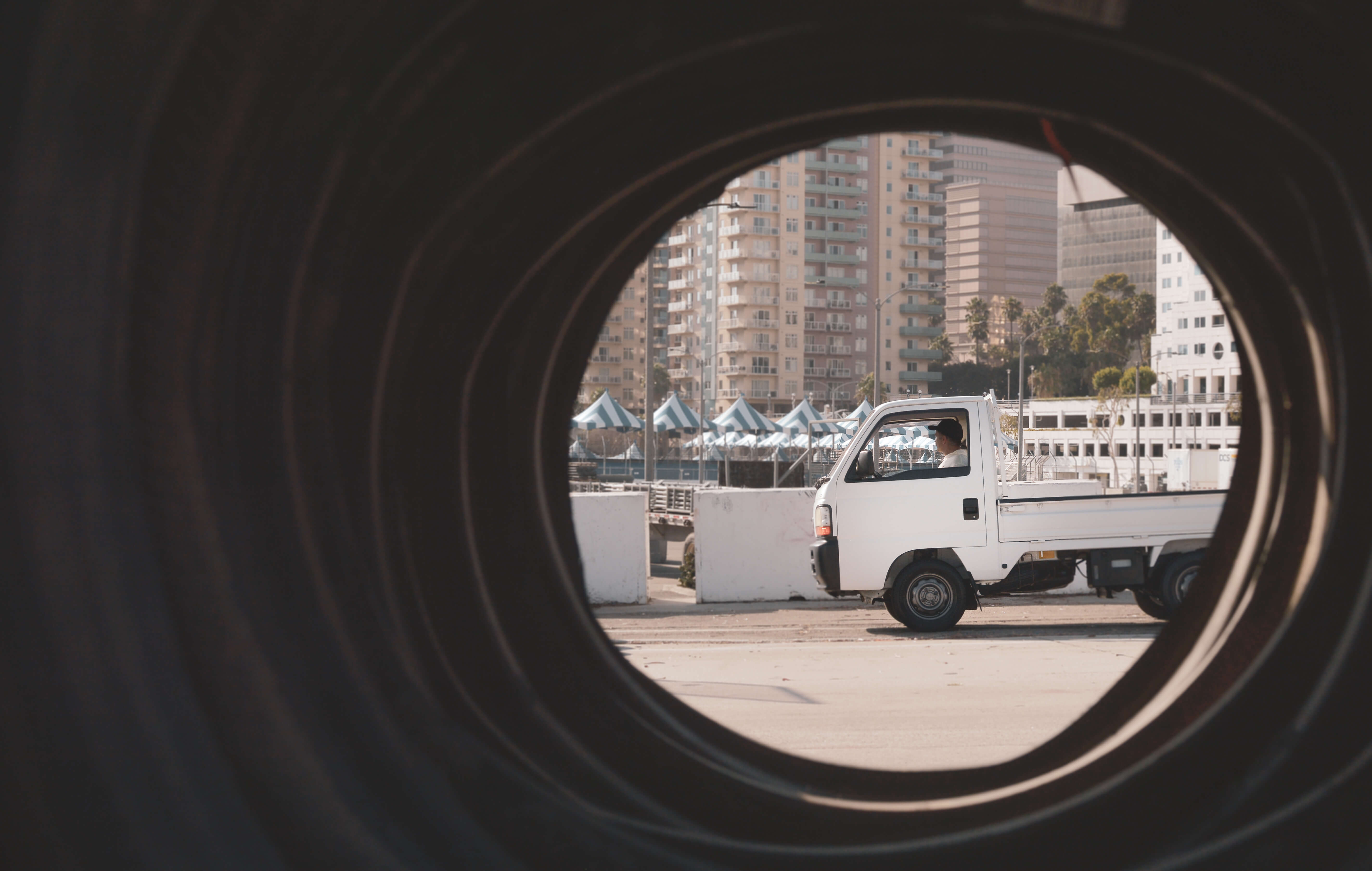 A white pickup truck framed by a tire in an urban setting, showcasing the new kei truck's compact design and innovation.