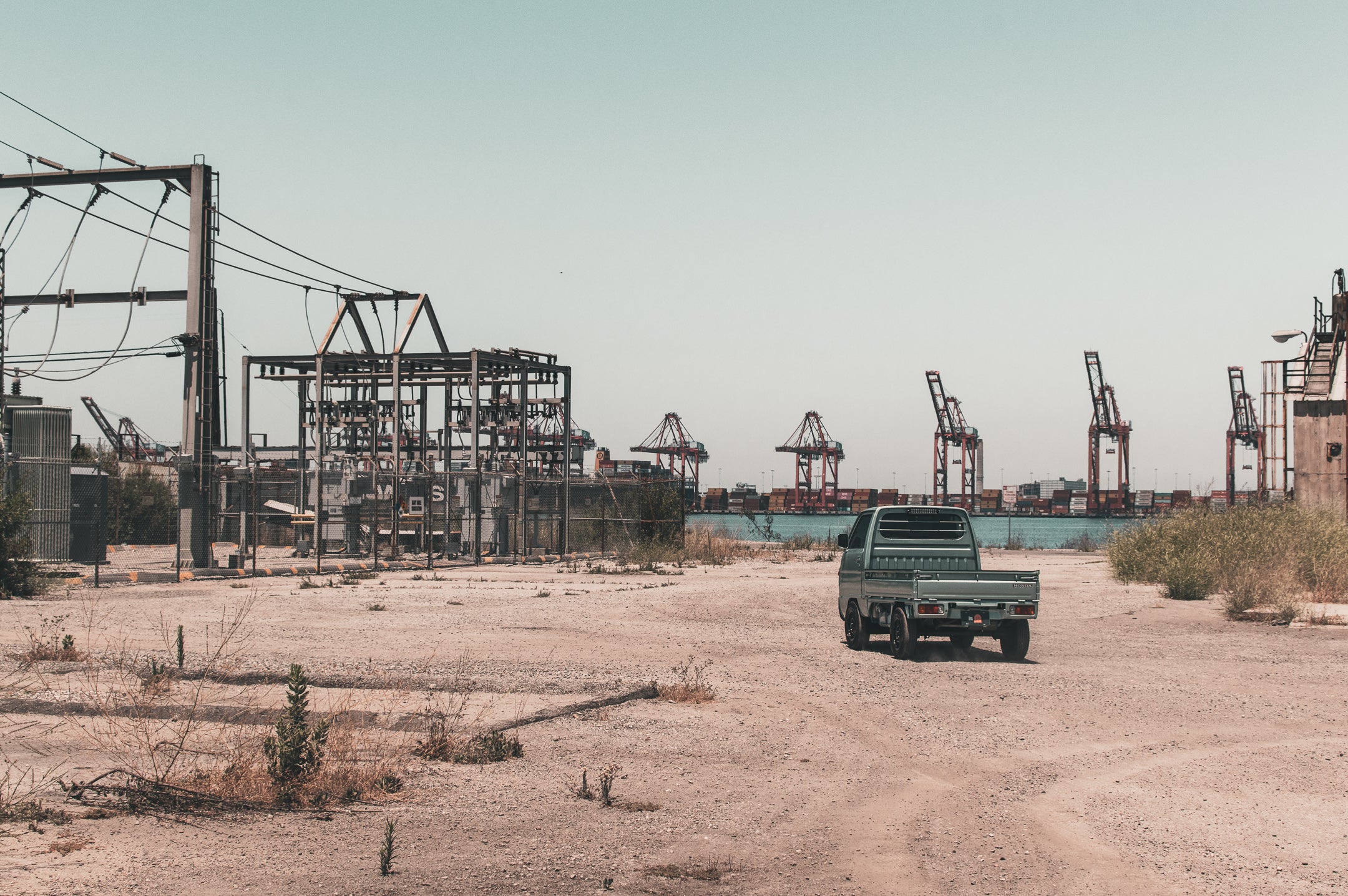 A 4x4 kei truck traversing a rugged dirt road in an industrial area, showcasing its off-road capabilities.