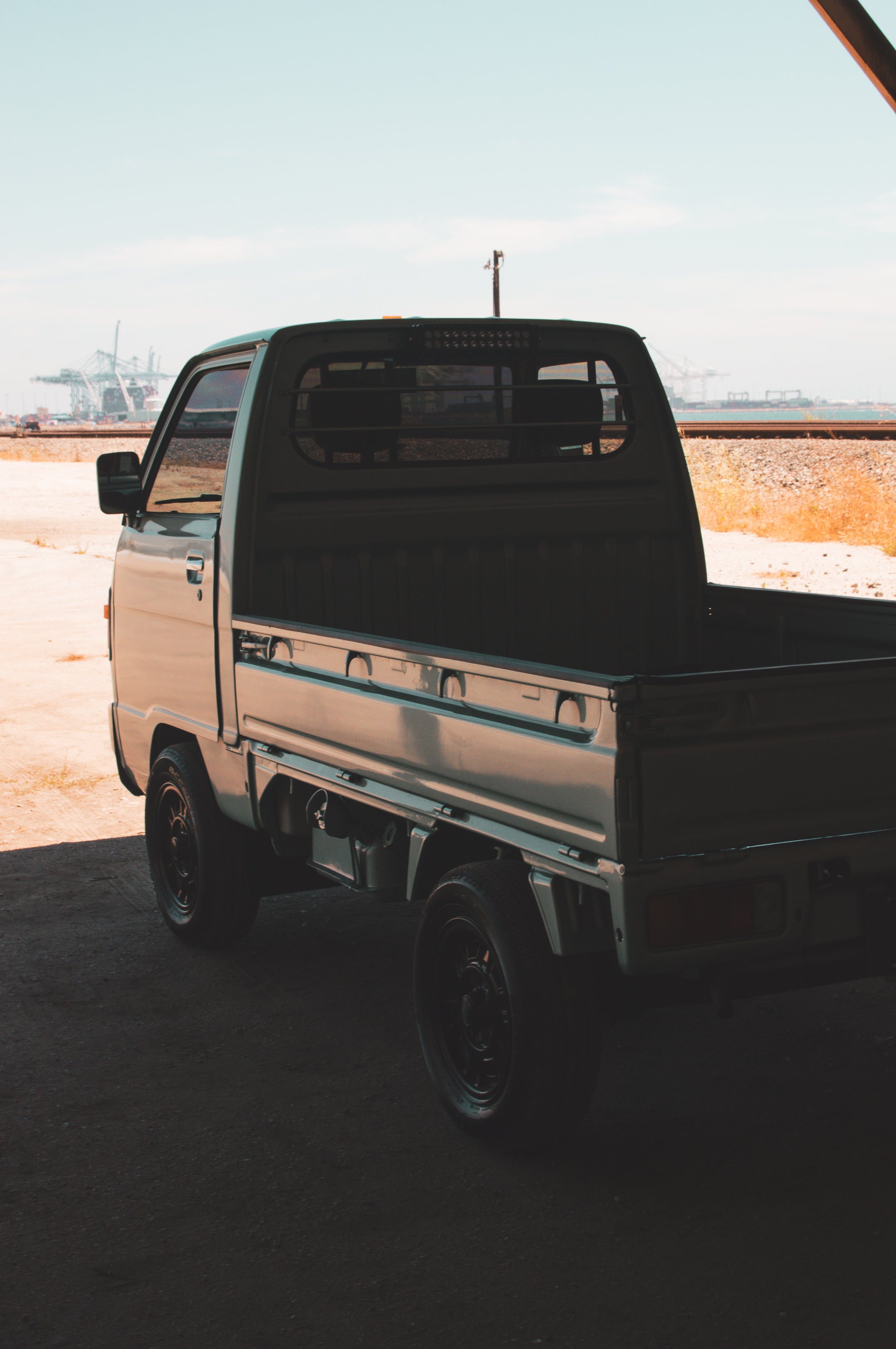 Kei truck dump bed in an industrial setting with cranes and blue sky.