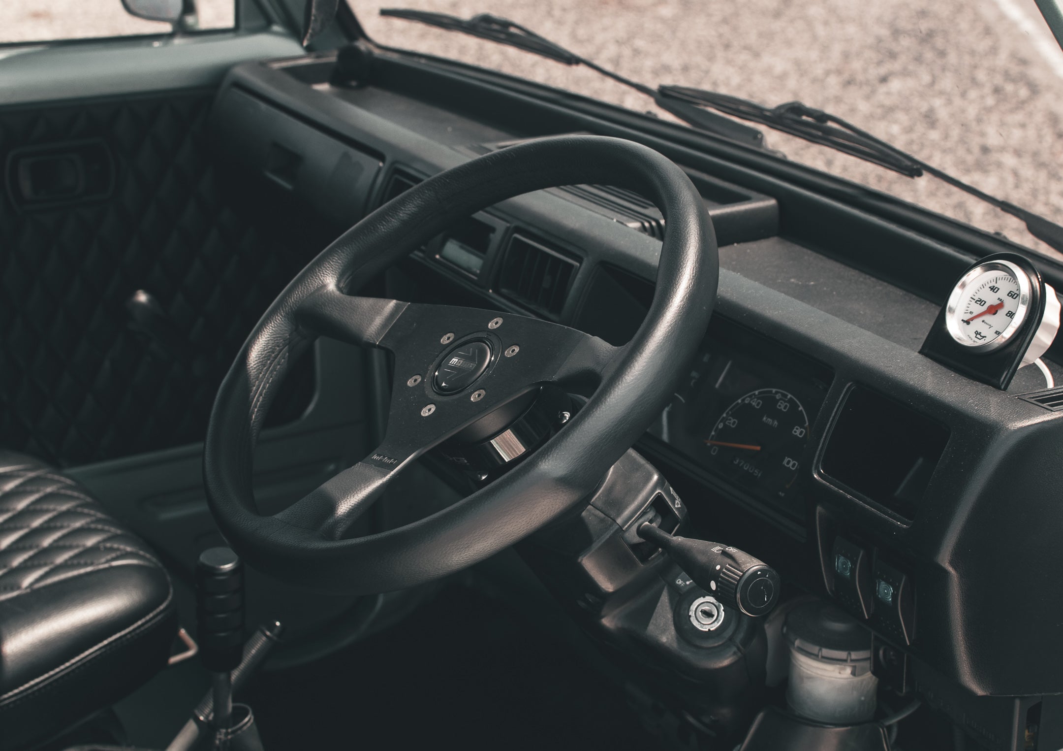 Interior view of a kei truck showcasing the steering wheel, dashboard, and quilted seat pattern, highlighting its compact and vintage design.