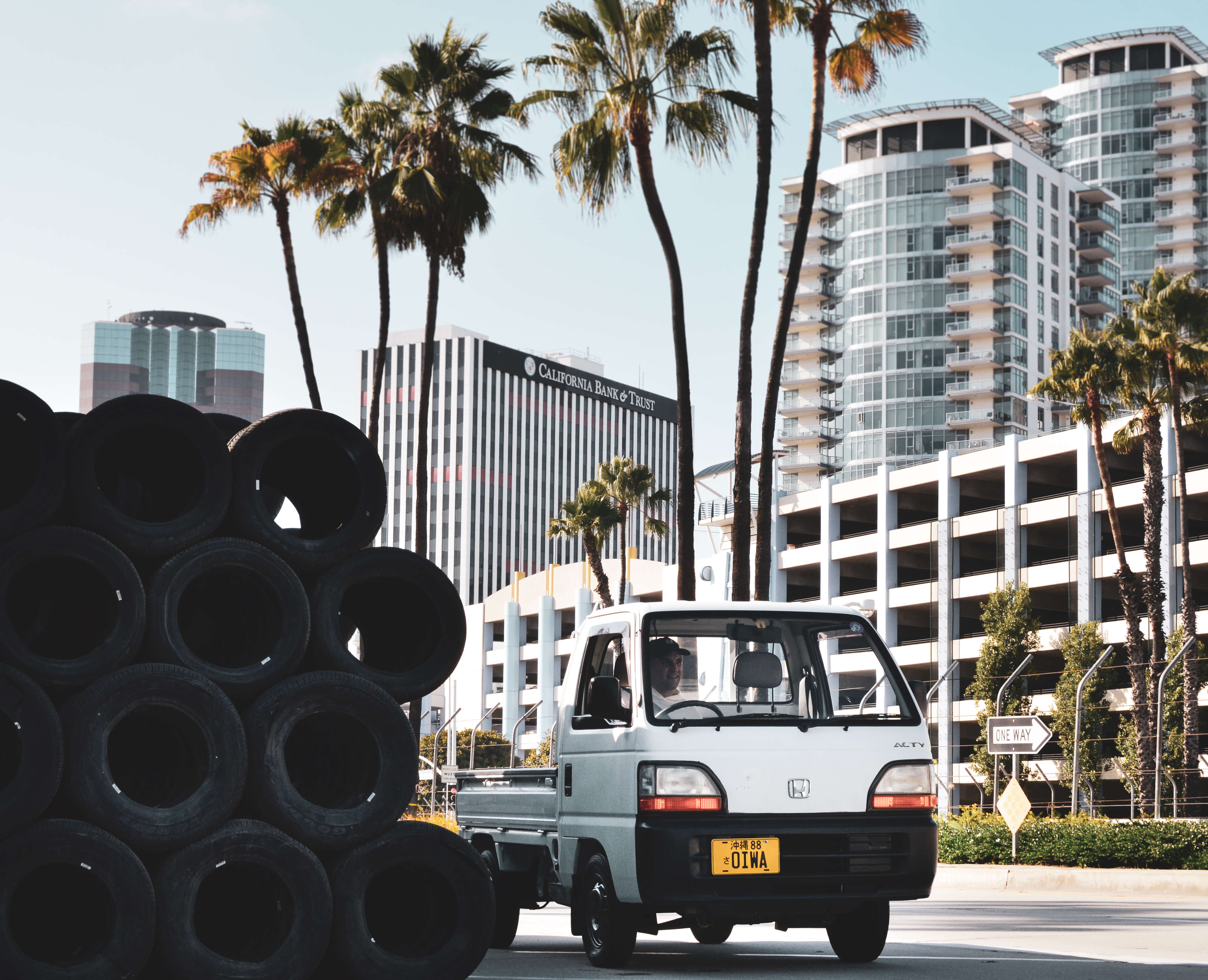 A kei truck driving on a palm-lined street with tall buildings in the background, showcasing urban mobility and efficiency.