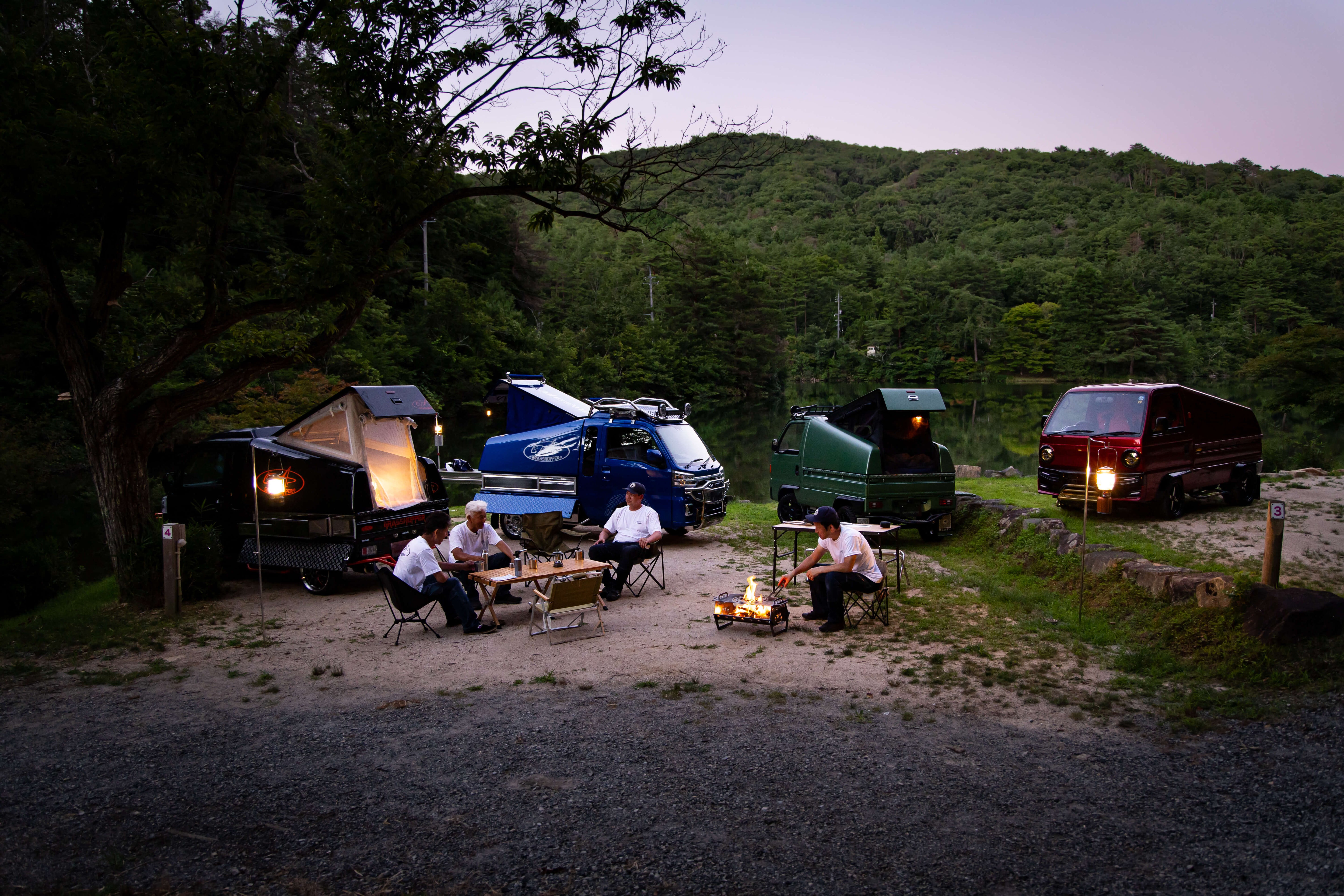 Kei trucks with body kits in a serene outdoor setting, featuring camping setups and vibrant colors.