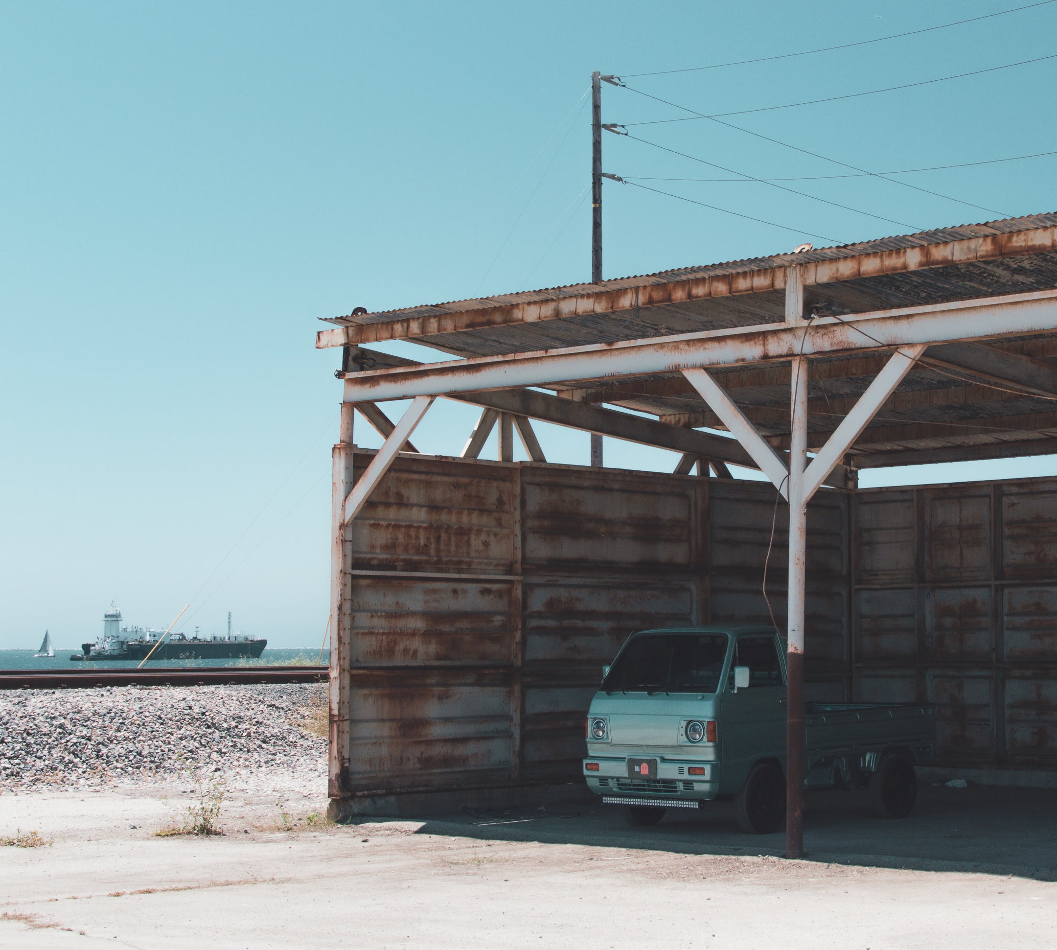 A light blue kei truck parked in an open metal structure near a large ship, symbolizing the journey from Japan to Ohio.