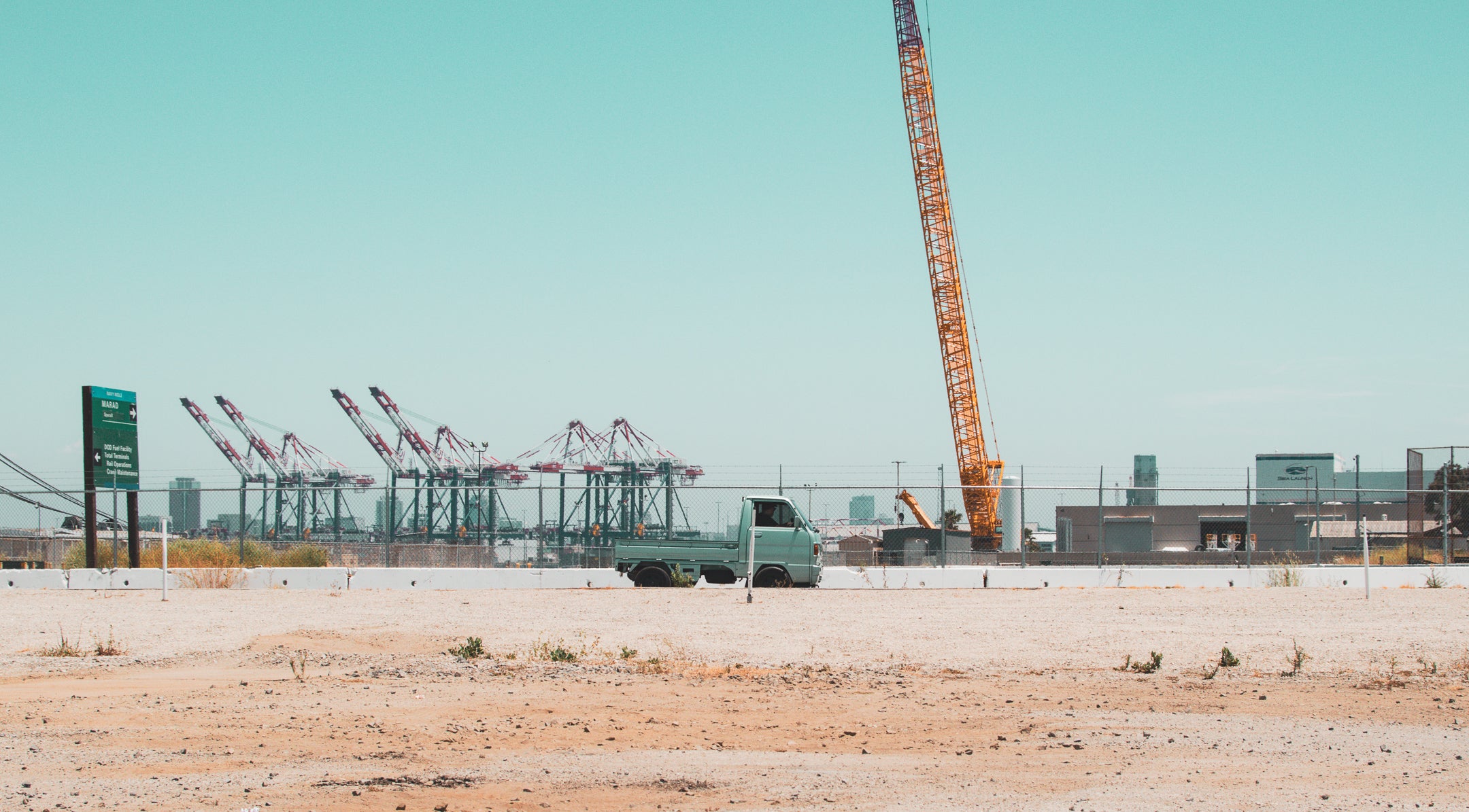 A blue kei truck at a construction site with cranes in the background, showcasing Japanese engineering.