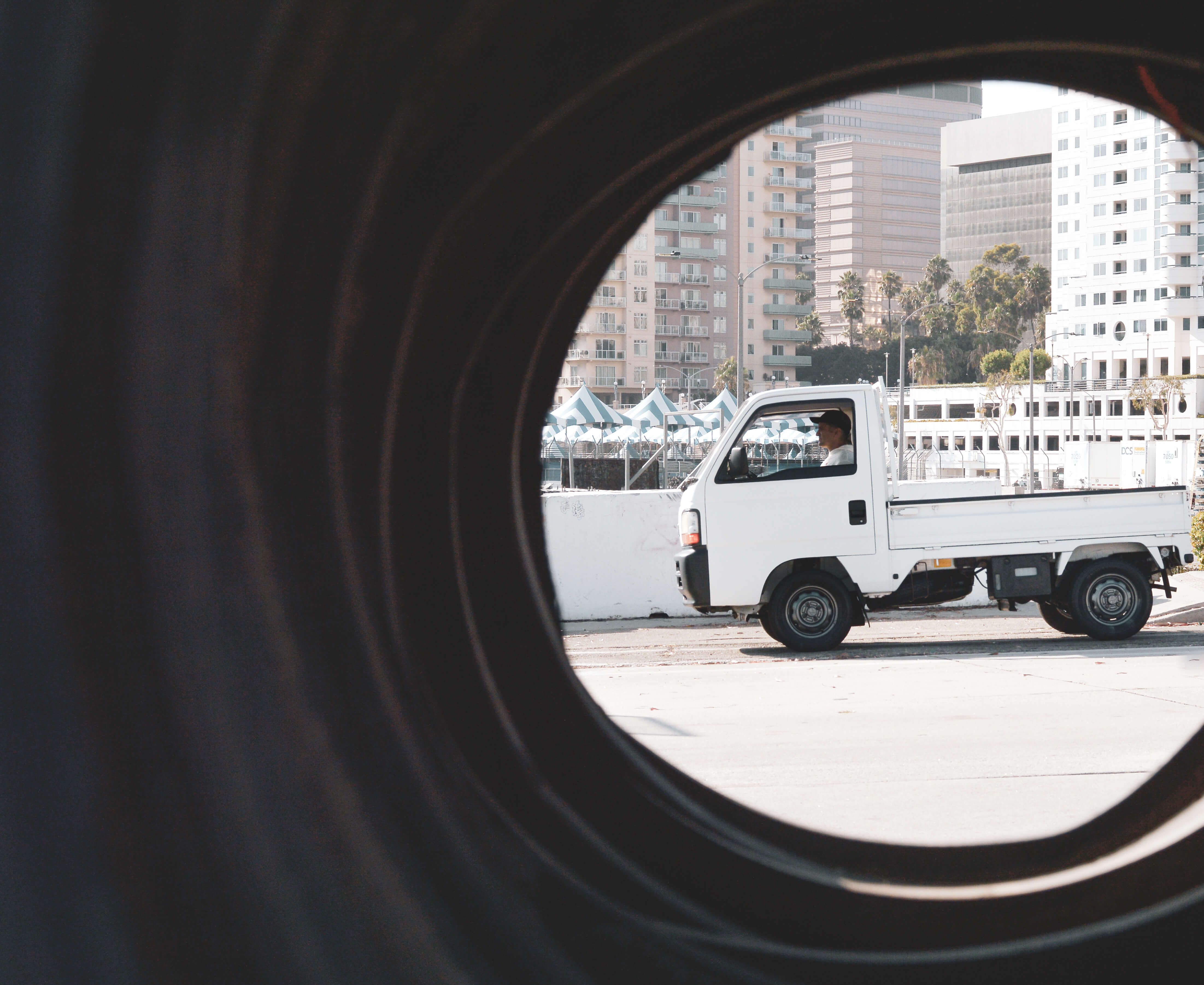 Kei truck vs F150: A white pickup truck framed by a tire, urban backdrop.