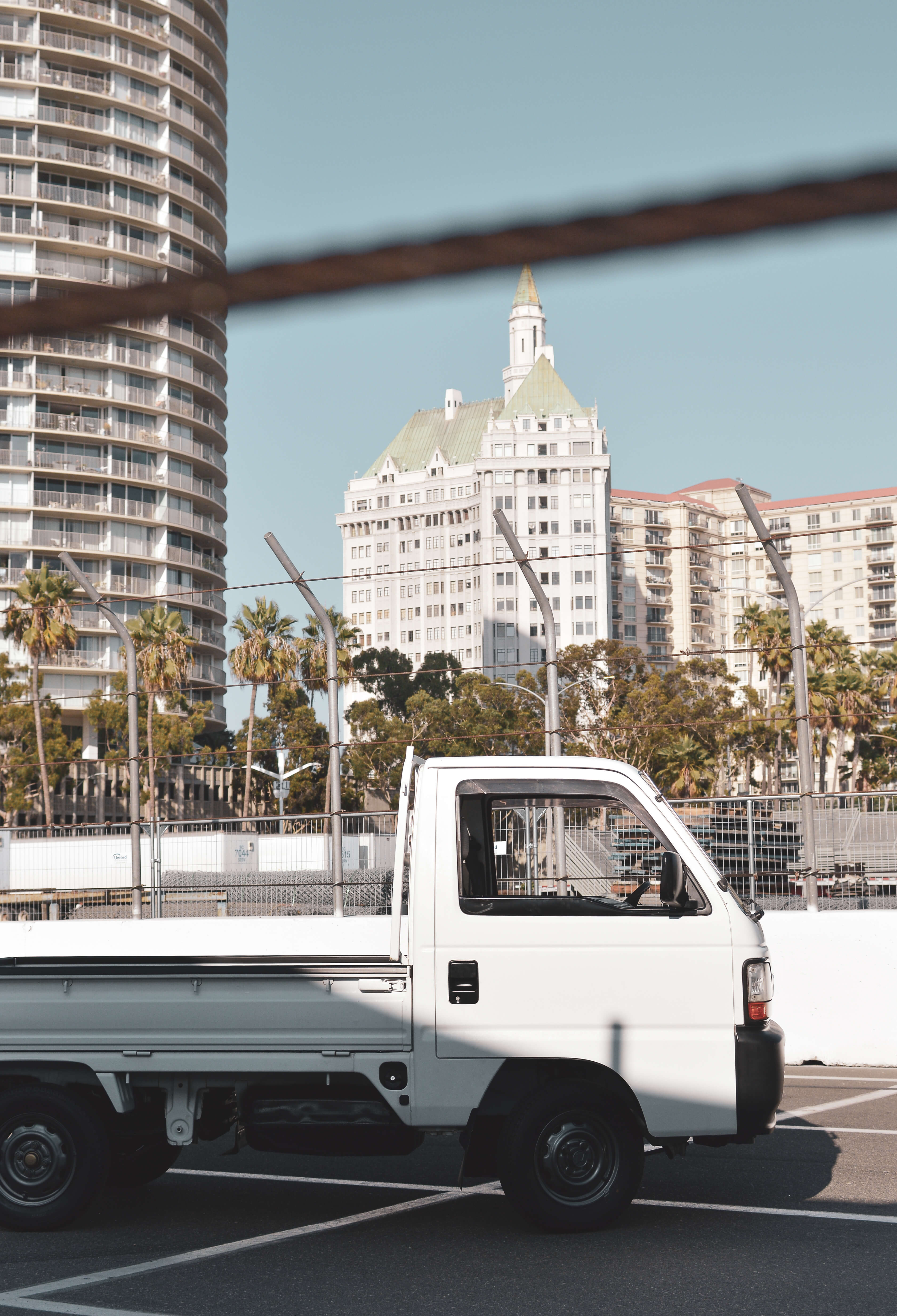 New kei truck parked on a paved surface, showcasing modern features with a backdrop of urban architecture and clear blue sky.