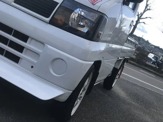 White U61T Mitsubishi Minicab Kei truck featuring a custom body kit and front bumper detail in an outdoor setting