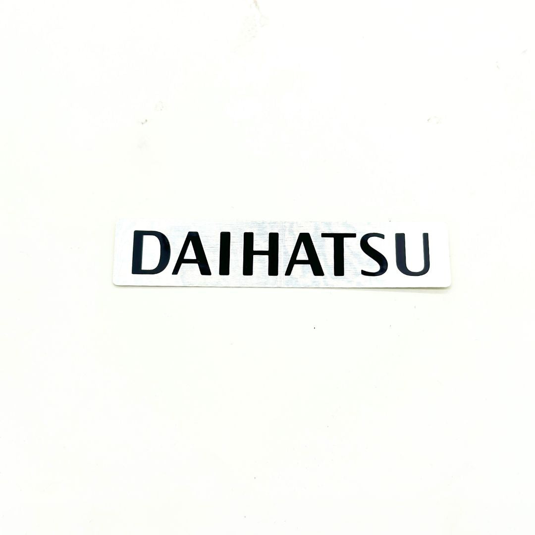 Daihatsu Hijet Truck S500P, 510P (2014-Present) OEM-style brushed aluminum tailgate decal strip featuring bold black “DAIHATSU” lettering for authentic exterior branding – Decal Parts collection.