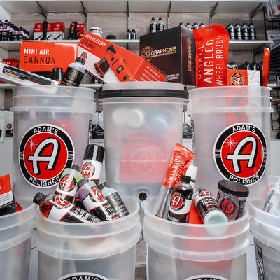 Adam’s Polishes car detailing essentials for Kei Trucks displayed in branded clear buckets, featuring premium accessories like the Mini Air Cannon, Angled Wheel Brush, and graphene-infused products for top-tier automotive cleaning and protection.