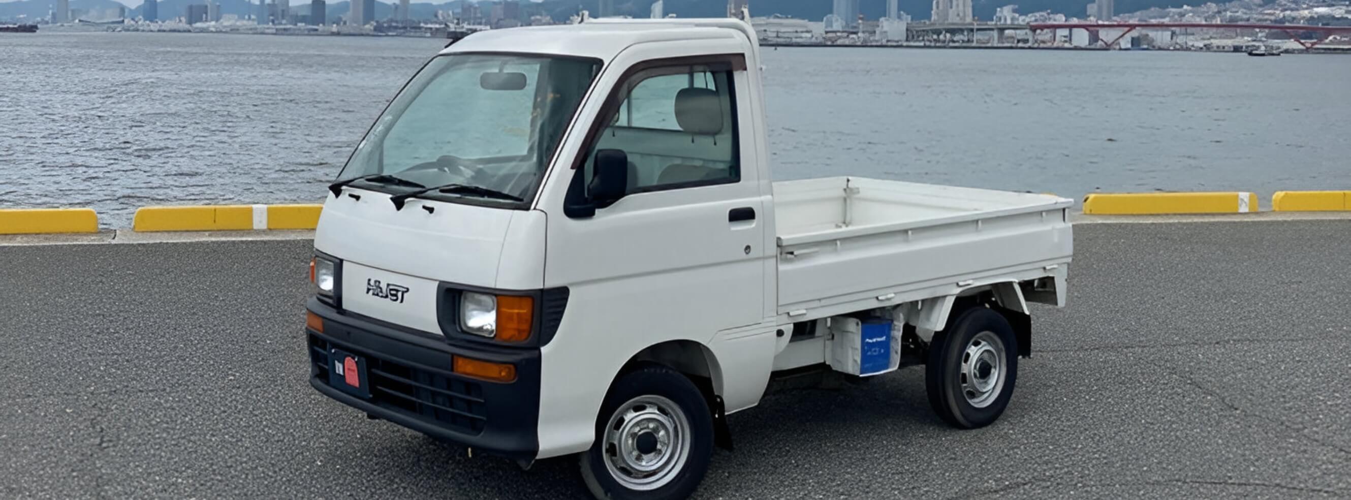 Daihatsu Hijet kei truck parked near the water, showcasing its compact yet versatile design. Ideal for farm work, small deliveries, and off-road tasks, this reliable mini truck is a popular choice for both professional and personal use.