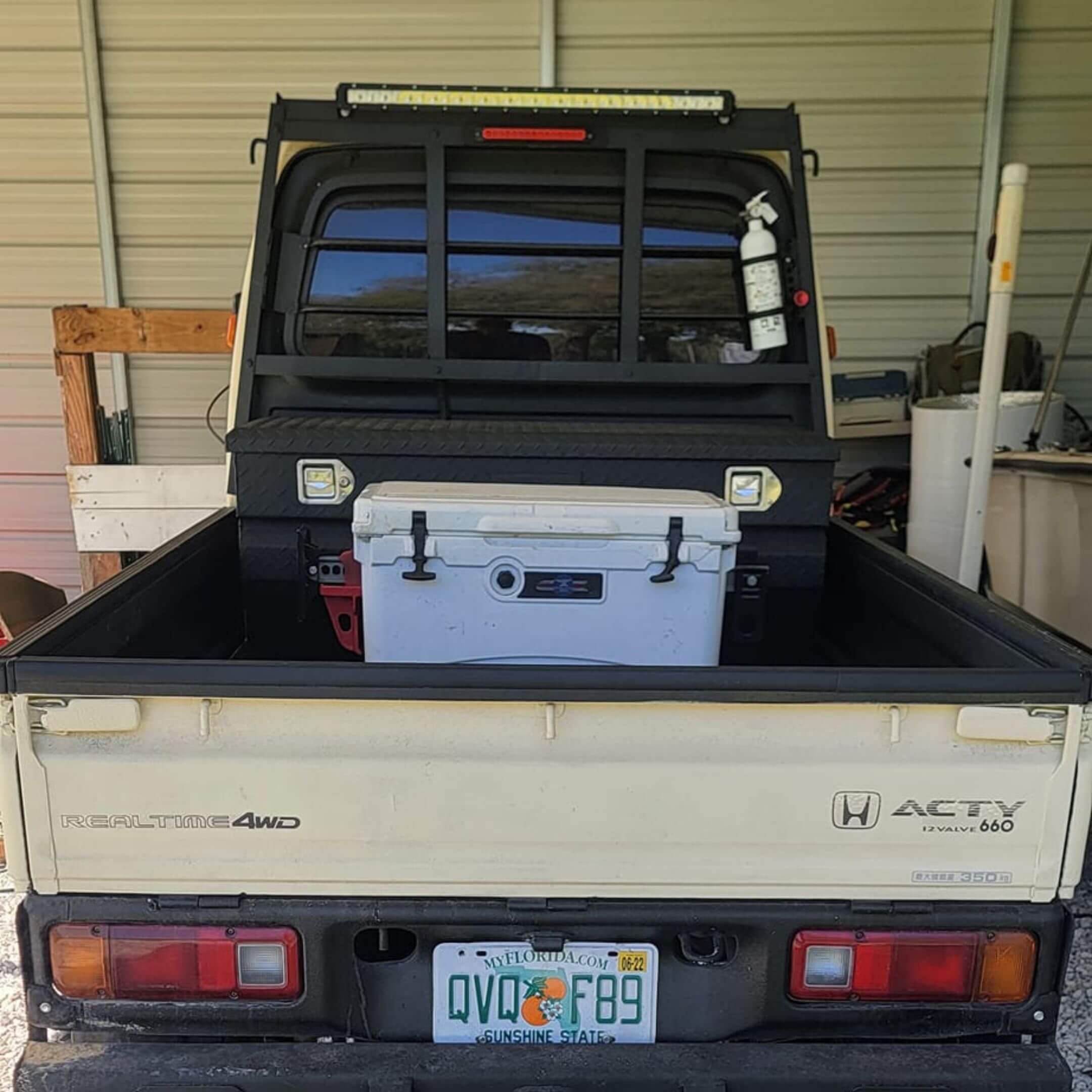 Rear cargo area of a Honda Acty truck equipped with tools and a cooler, demonstrating the vehicle’s utility and cargo space.