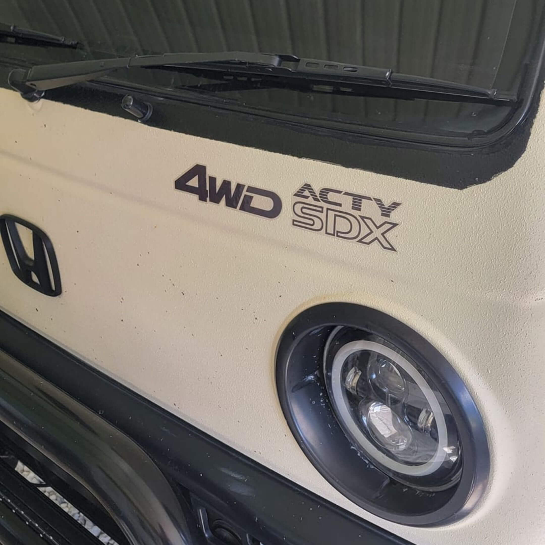 Detailed view of a 4WD ACTY SDX decal on a white Honda Acty, emphasizing the truck's four-wheel drive features.