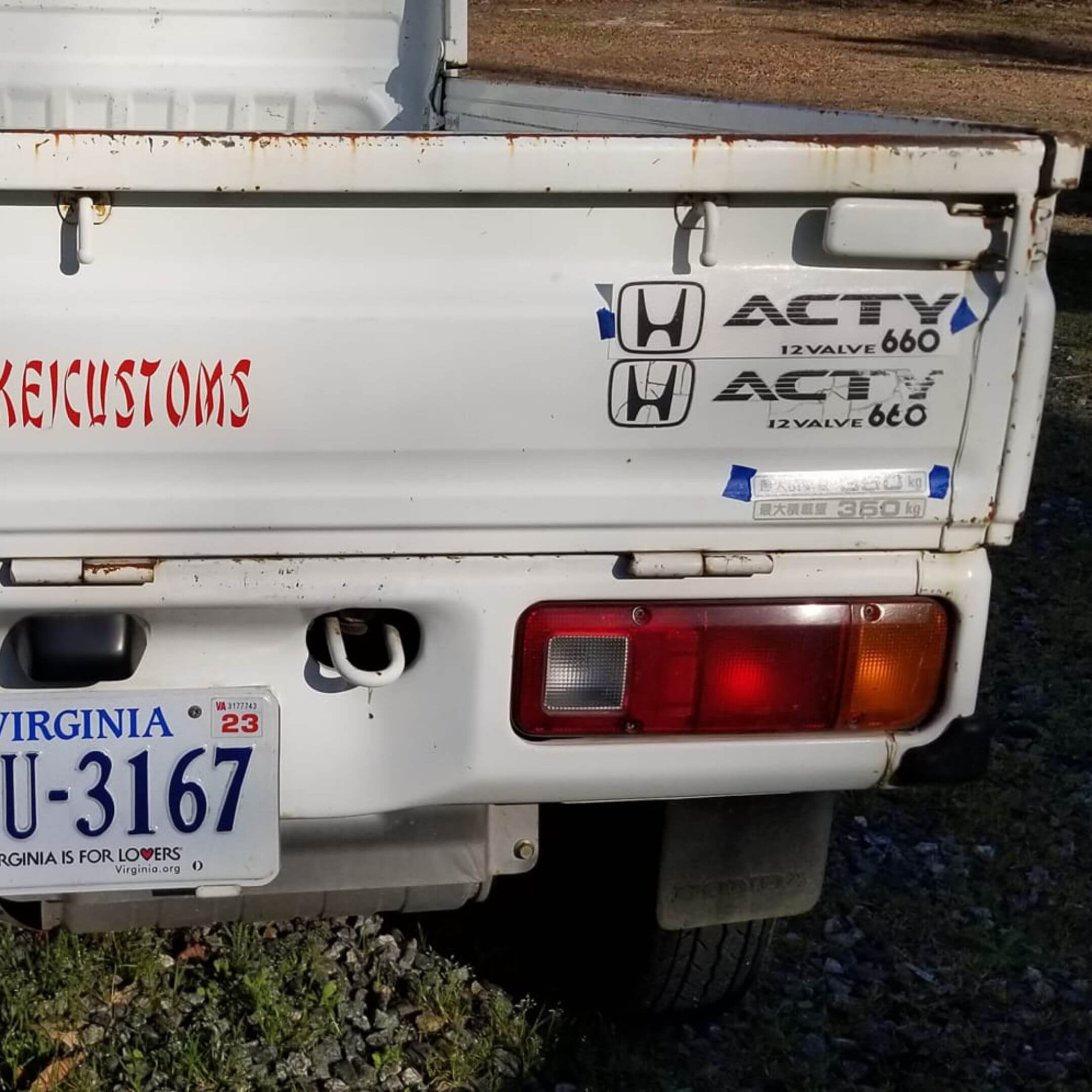 Detailed shot of a weathered white Honda Acty displaying a REALTIME 4WD decal, suitable for highlighting rugged design elements.