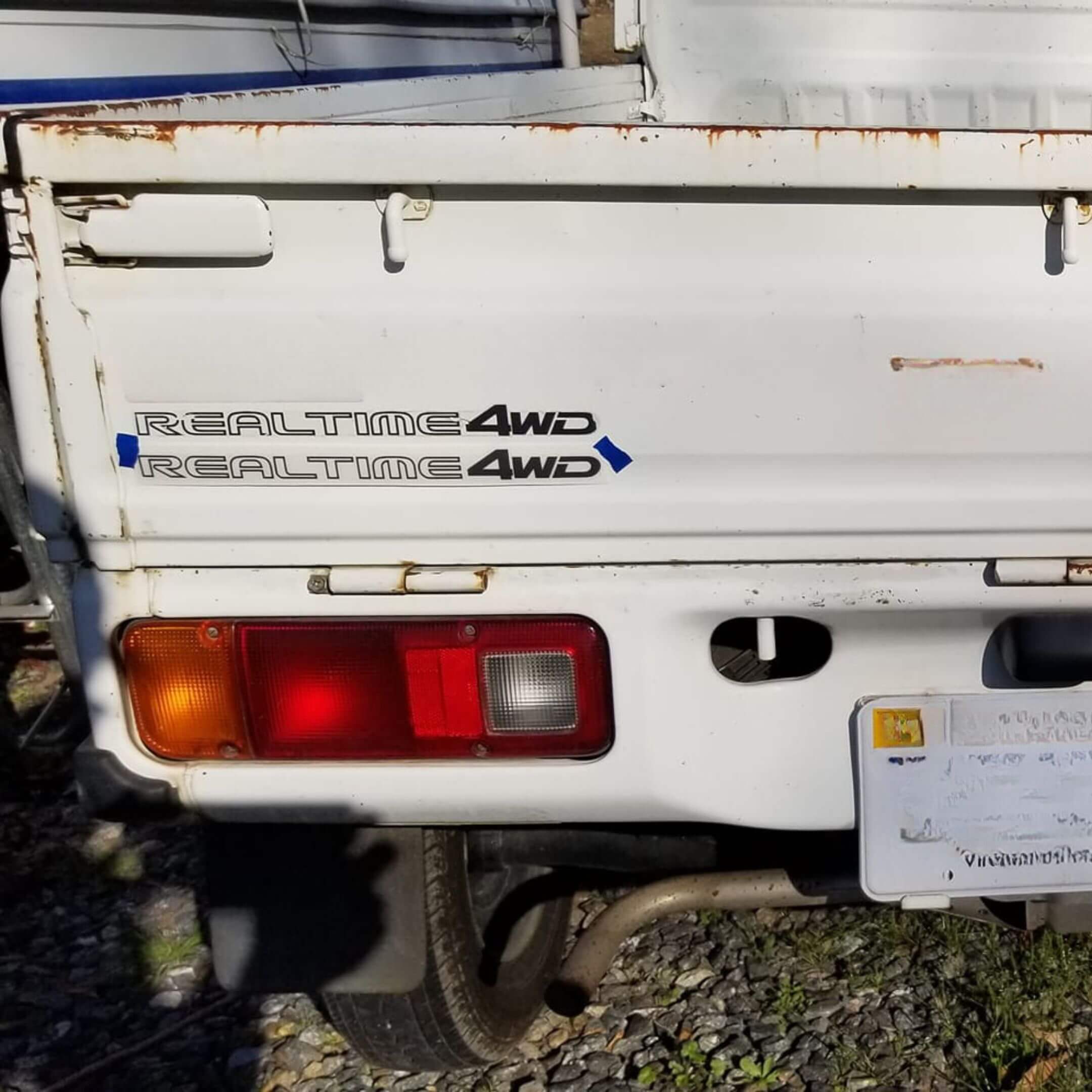 Detailed shot of a weathered white Honda Acty displaying a REALTIME 4WD decal, suitable for highlighting rugged design elements.