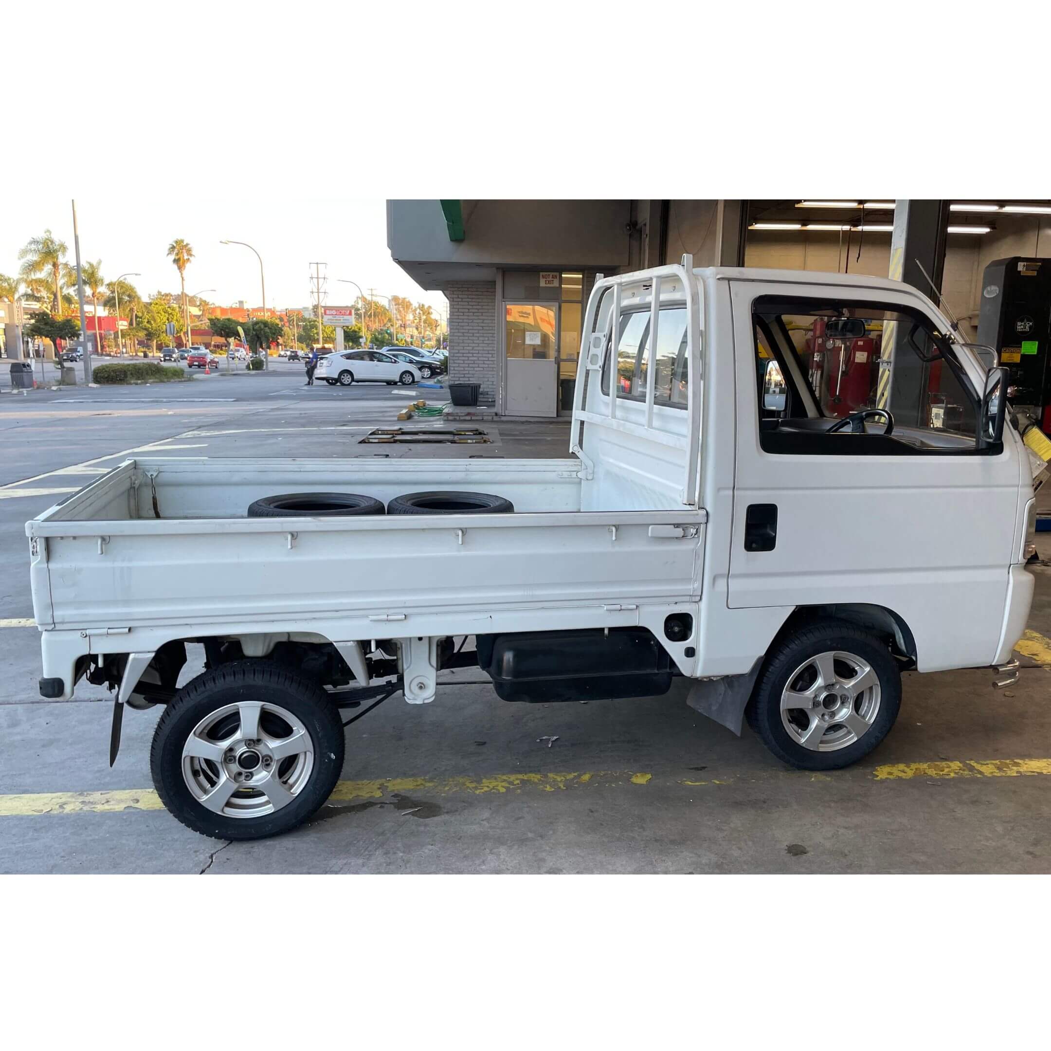 Driver-side profile of white 1994 Honda Acty Town 4WD mini truck, parked at service area showing clear bed space and tire condition.