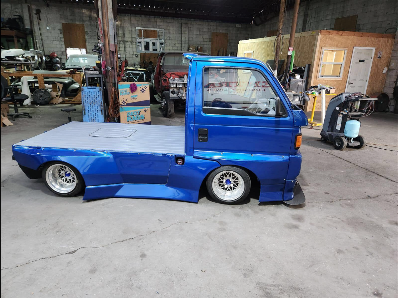 Classic Honda Acty mini truck enhanced with a white and black air suspension kit, parked outdoors highlighting its modified stance