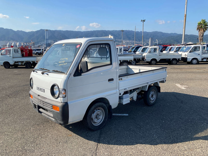 White 1994 Suzuki Carry Kei Truck parked outdoors, showcasing its compact size, round headlights, and flatbed design, ideal for utility and versatility, available at Oiwa Garage.