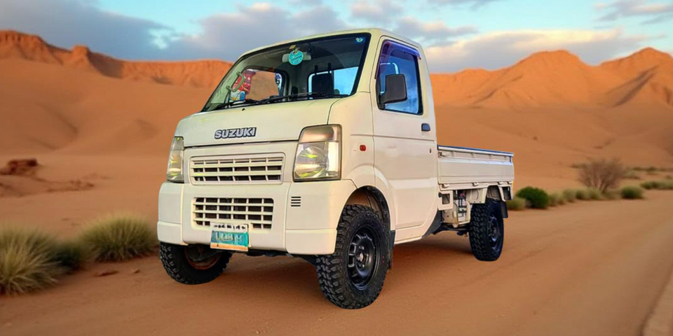 White Suzuki carry truck  in a desert landscape with mountains in the background