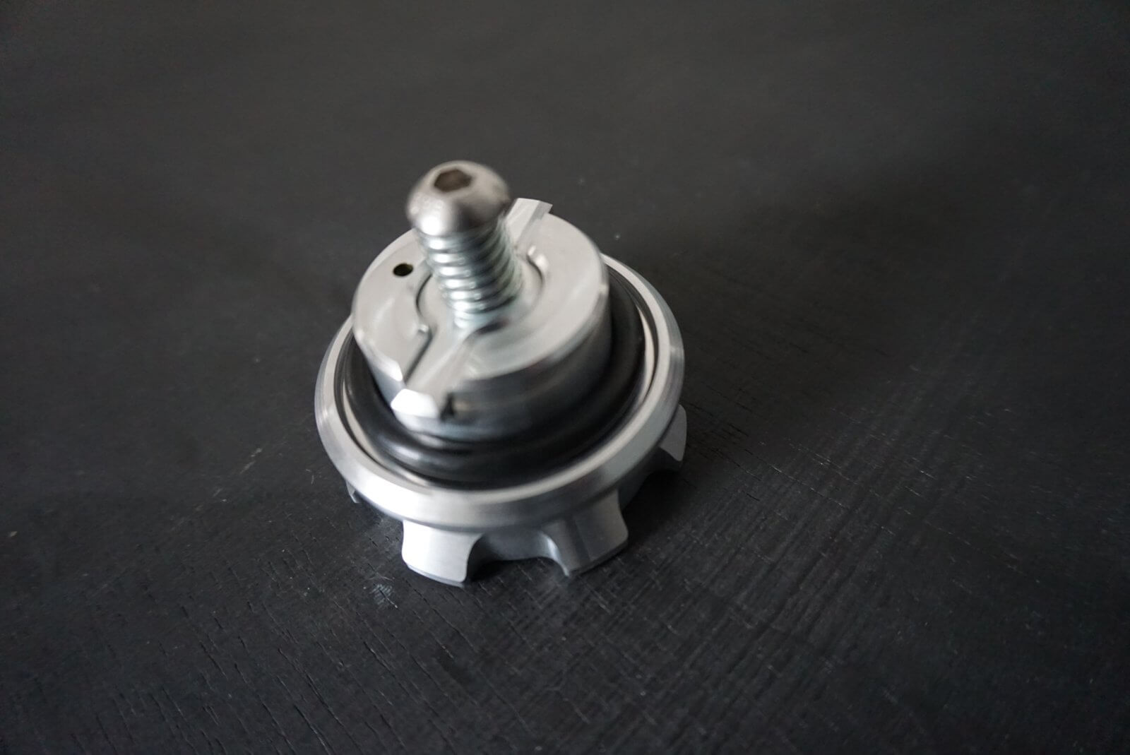 Crown gas cap for Honda Acty Truck, silver metal with rubber seal, angled view on a dark surface, highlighting details