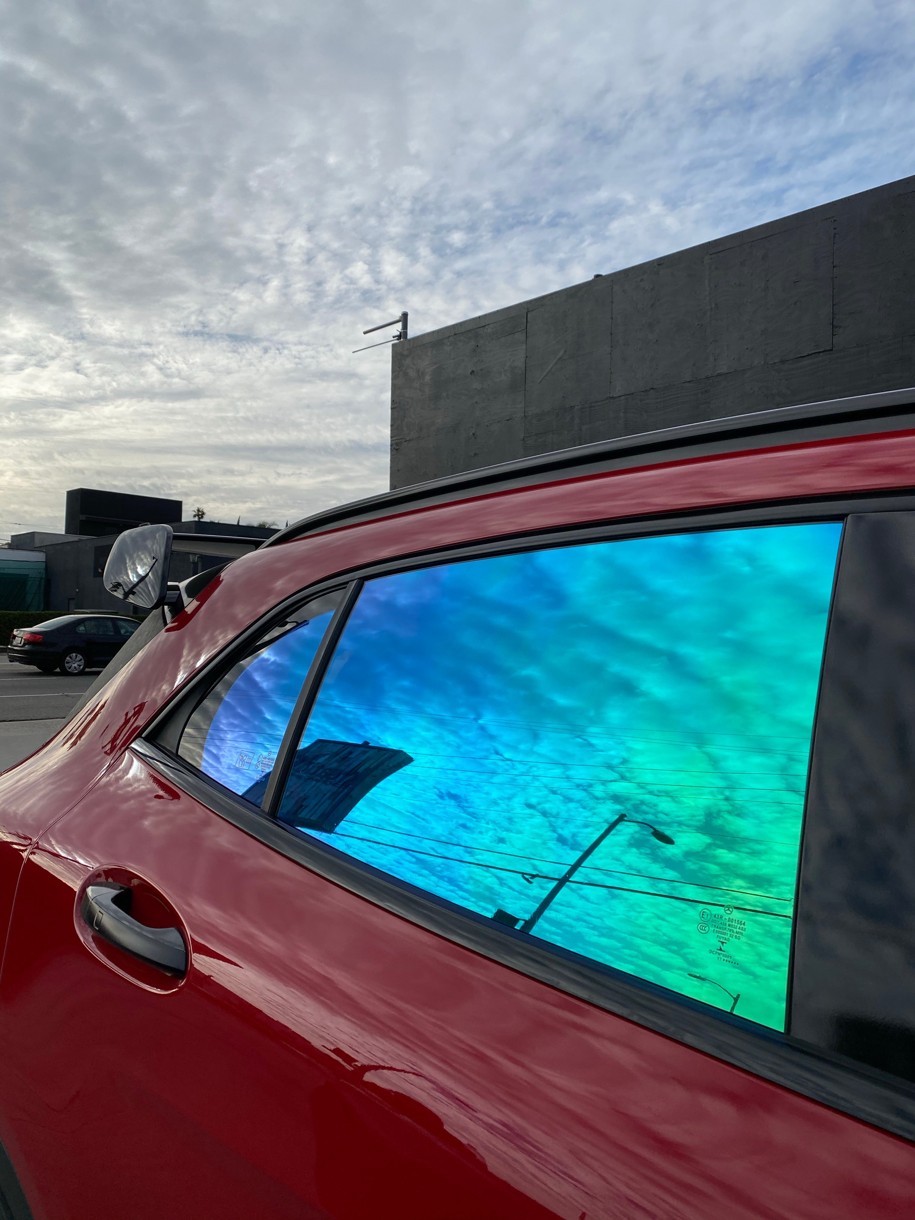 Red SUV with Opal colorshift ceramic tint by Omnique, displaying turquoise and blue reflections under sunlight.