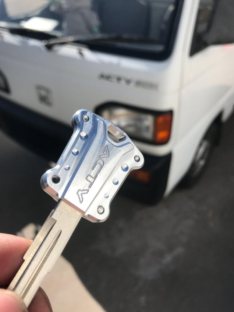 CNC-machined 6061 aluminum key cover for Honda Acty trucks, enhancing style with a durable upgrade, shown with a vehicle in the background.