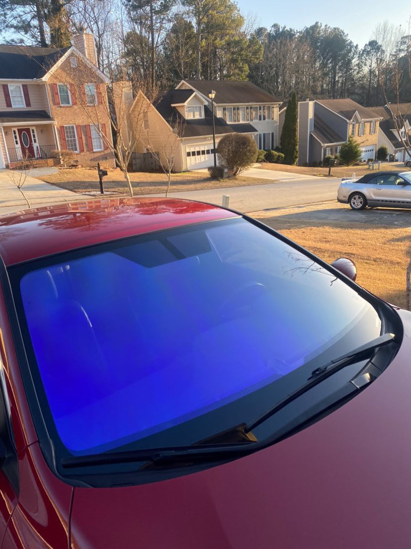 Red sedan equipped with Omnique IOLITE tint, showcasing sleek blue and purple colorshift in suburban neighborhood.