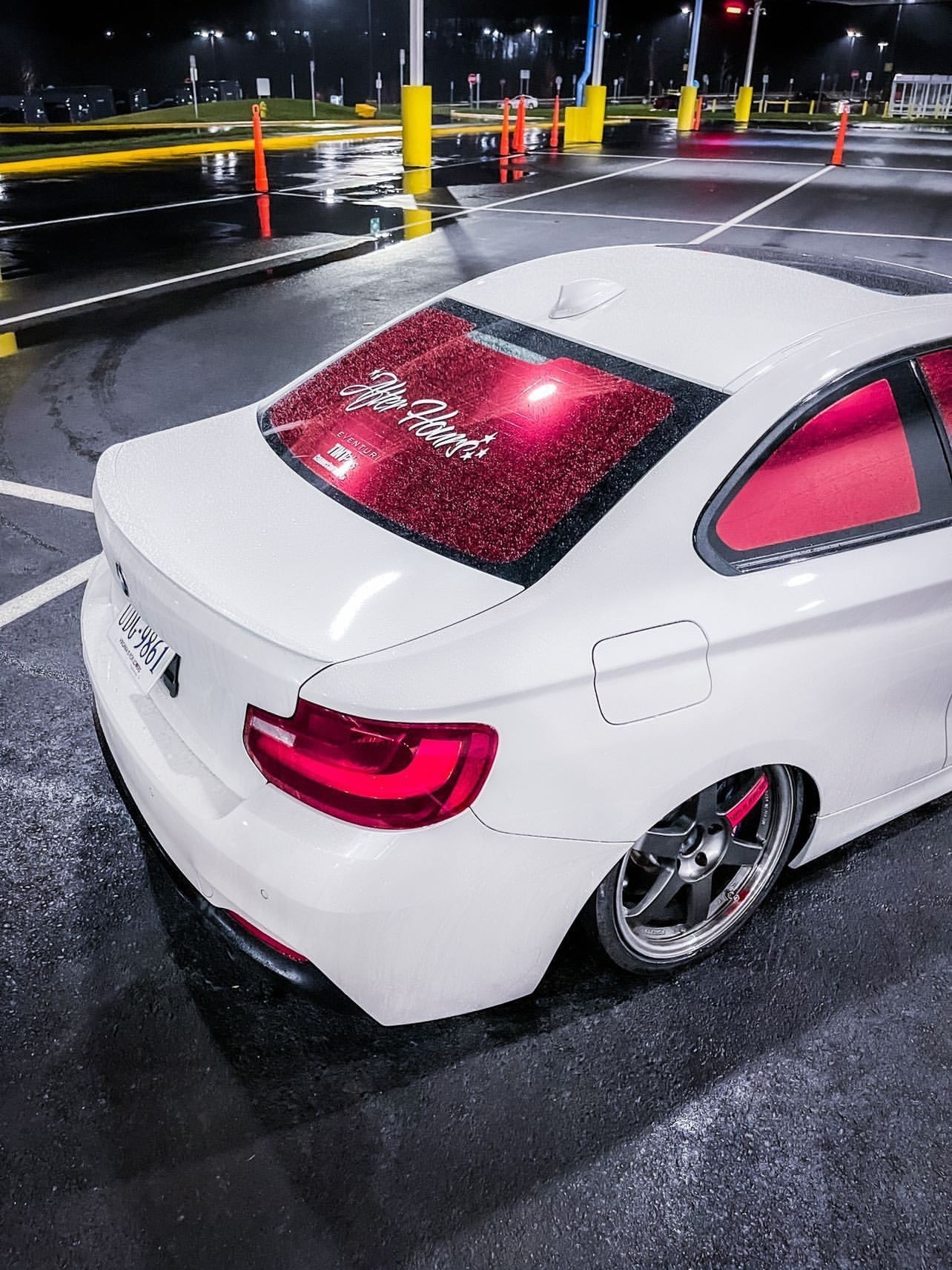 Omnique Vulcan Red tint on a white luxury car in a rainy evening parking lot.