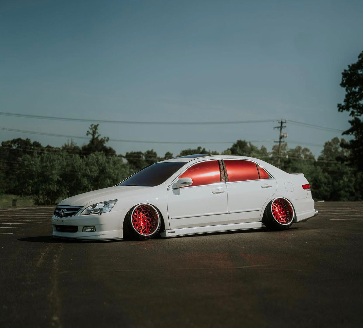 Custom white sedan with bold Vulcan Red tint windows, parked in a scenic area.