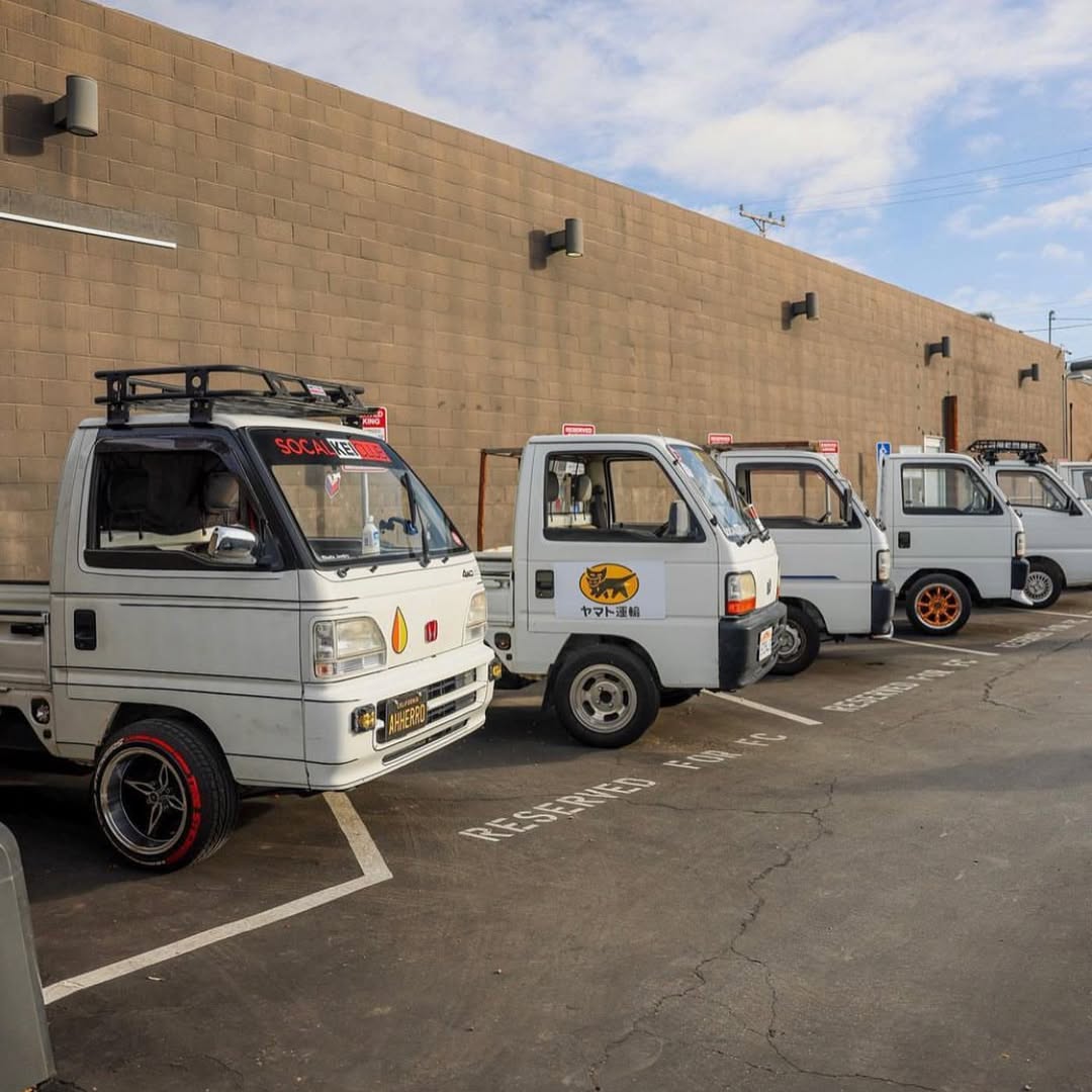 Lineup of Kei trucks including Subaru Sambar, Honda Acty, Daihatsu Hijet, and Suzuki Carry at a California meetup, showcasing custom wheels and street style.